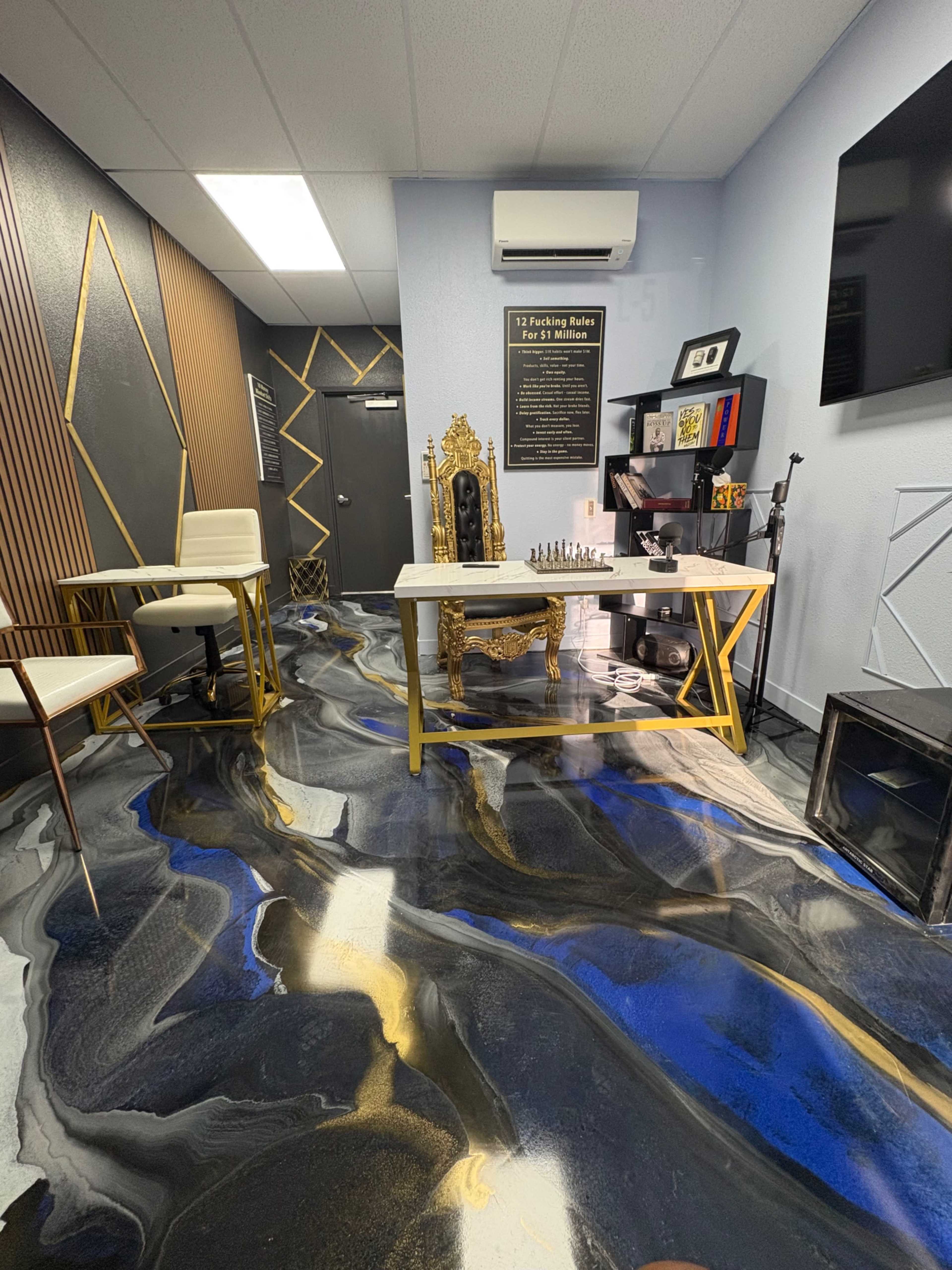 The image shows a modern room with a decorative floor featuring a blue, black, and gold pattern, a table with a chess set, a throne-like chair, and wall-mounted decor.