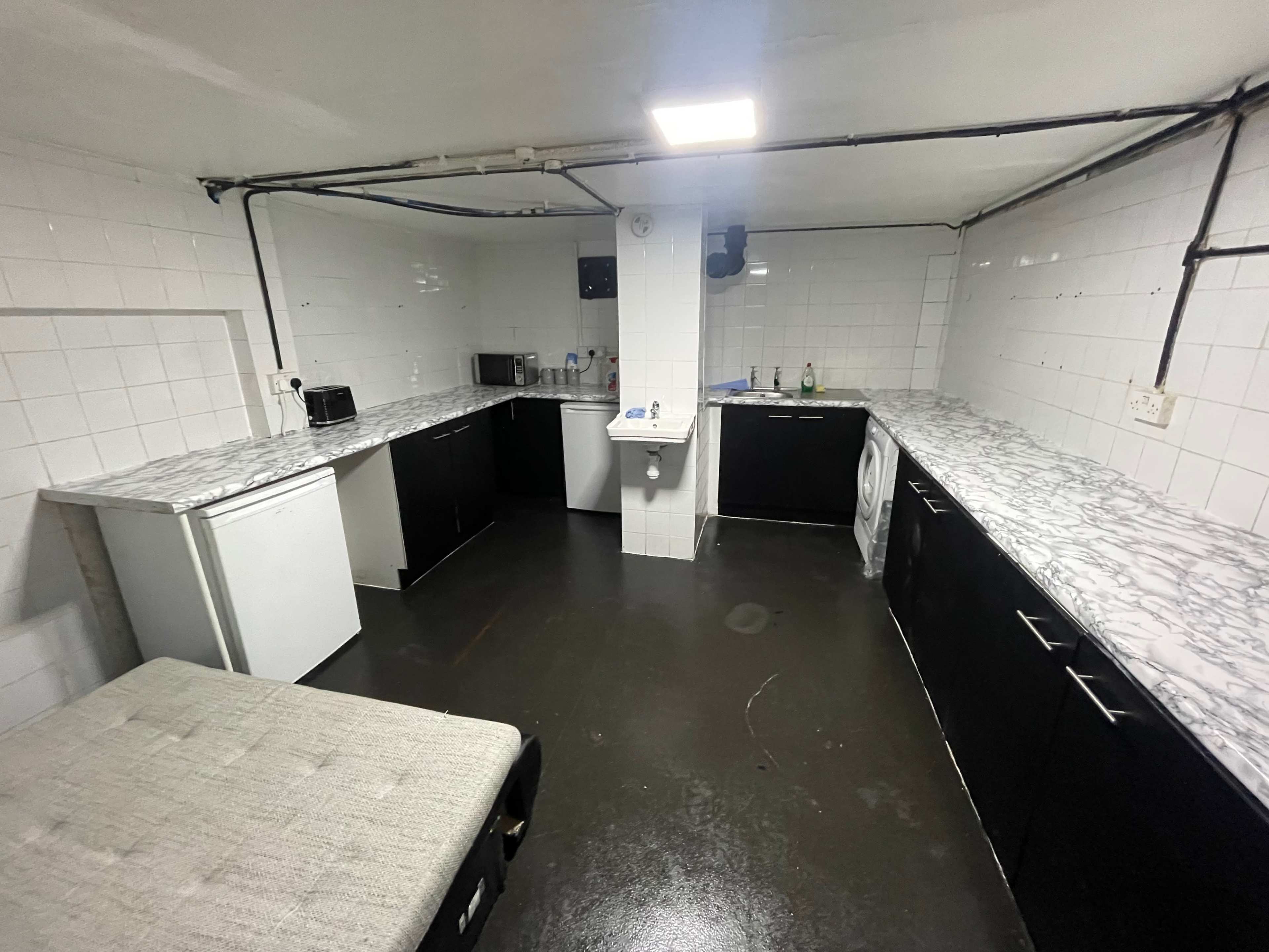 A spacious kitchen features marble countertops, black cabinets, and appliances against white tiled walls.