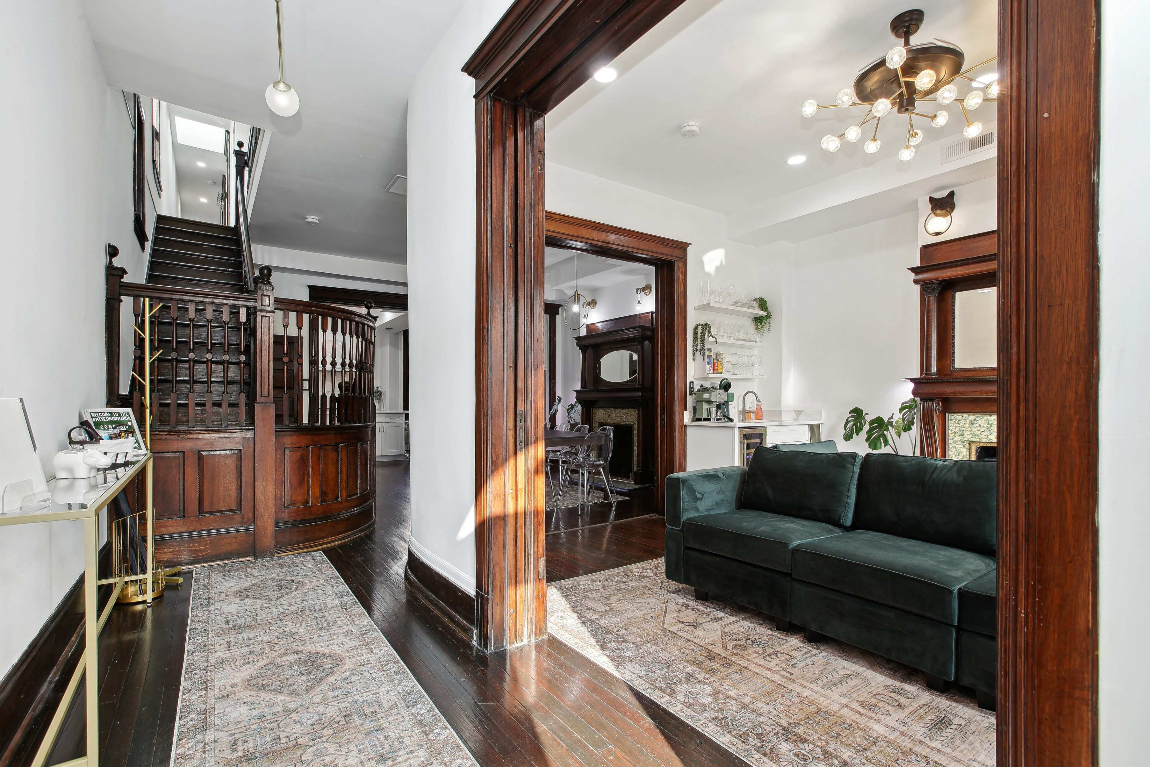 The image shows a spacious entryway leading to a staircase, with a dark wooden frame and a green couch positioned on a patterned rug.