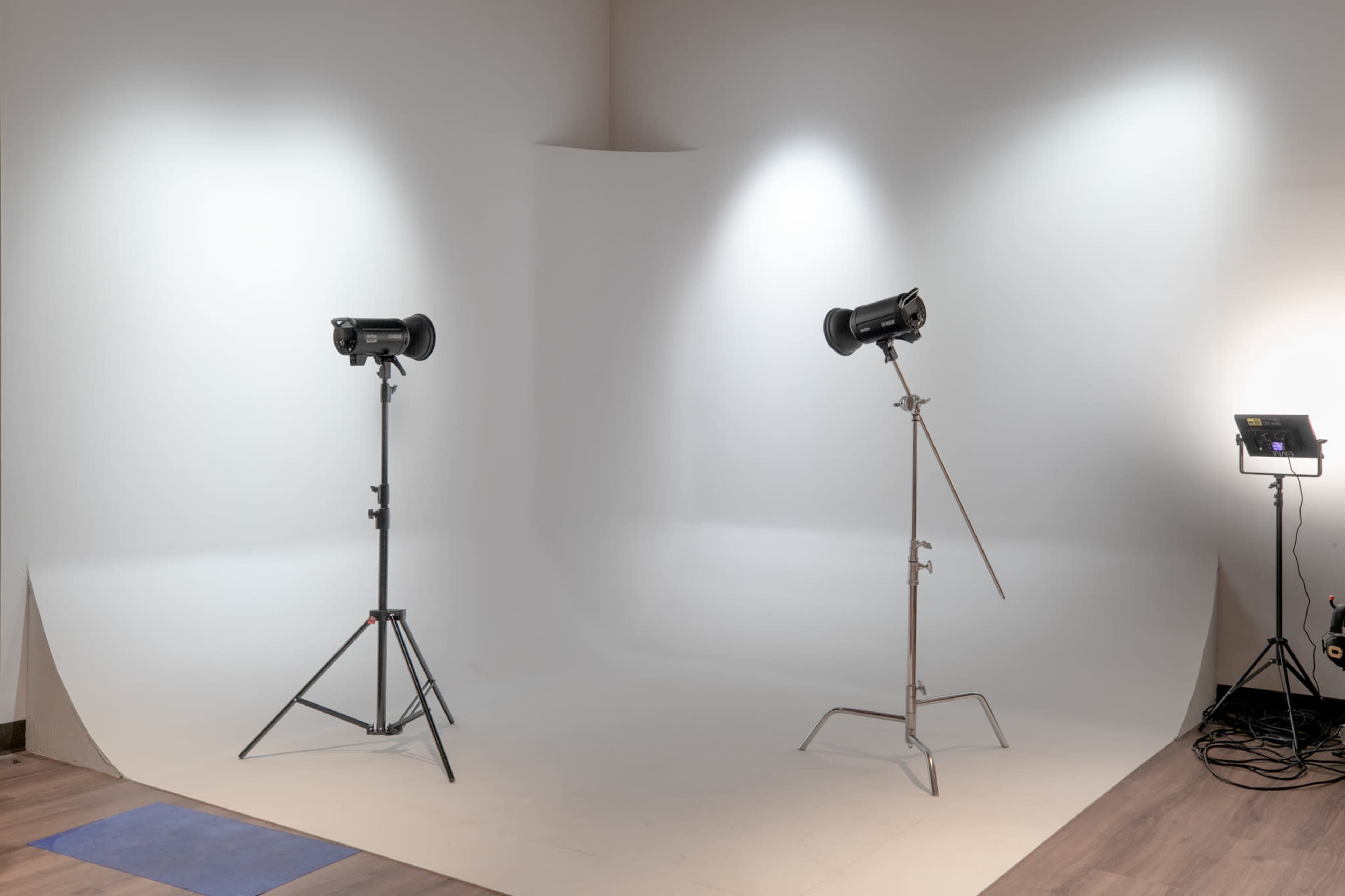 The image shows a photography studio setup with two light sources positioned on stands facing a white backdrop on the floor.