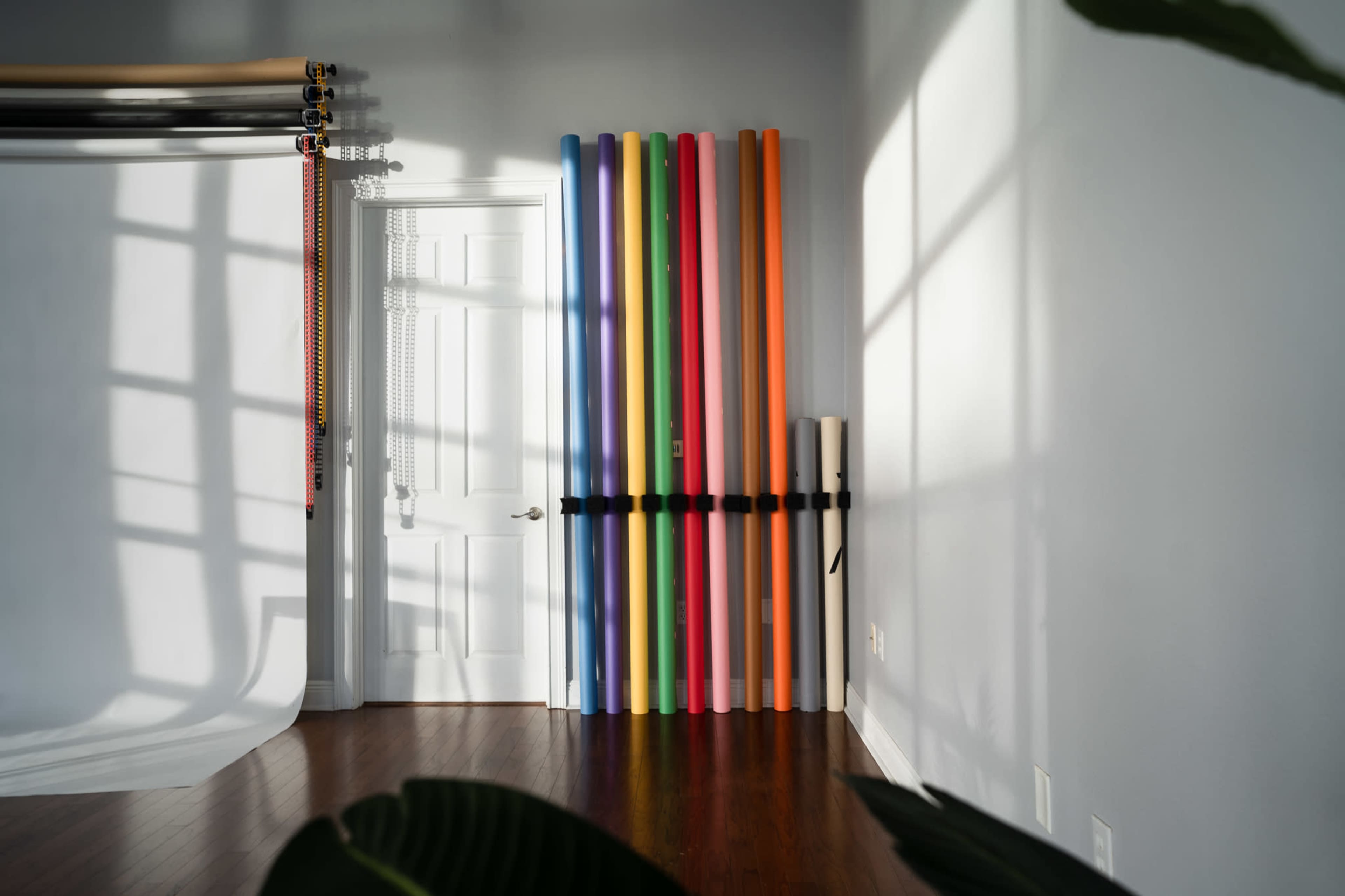 The image shows a well-lit room with a white door and vertical rolls of colored backdrop paper secured against a wall.