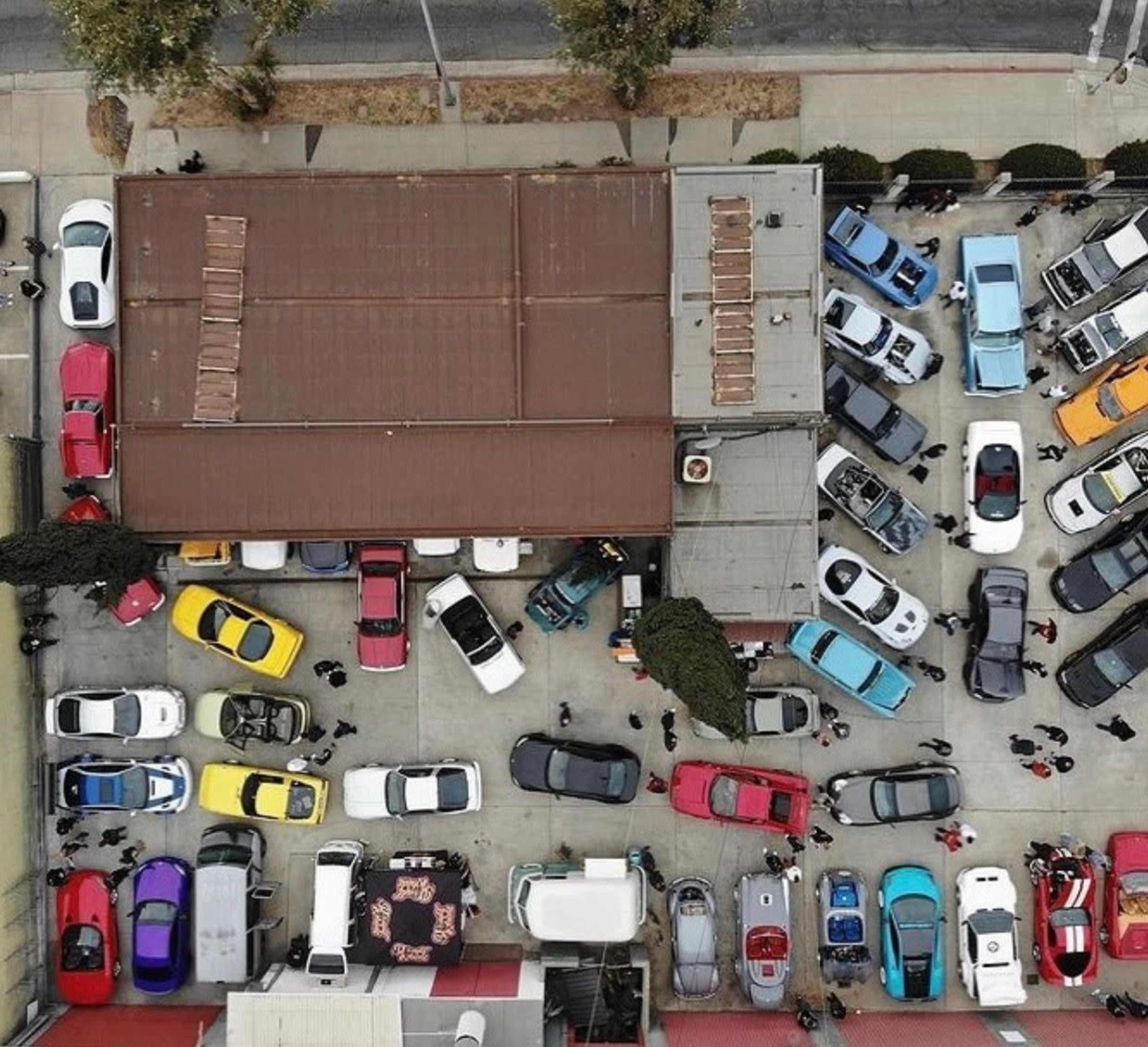 An aerial view of a crowded parking lot filled with various cars arranged around a central building.