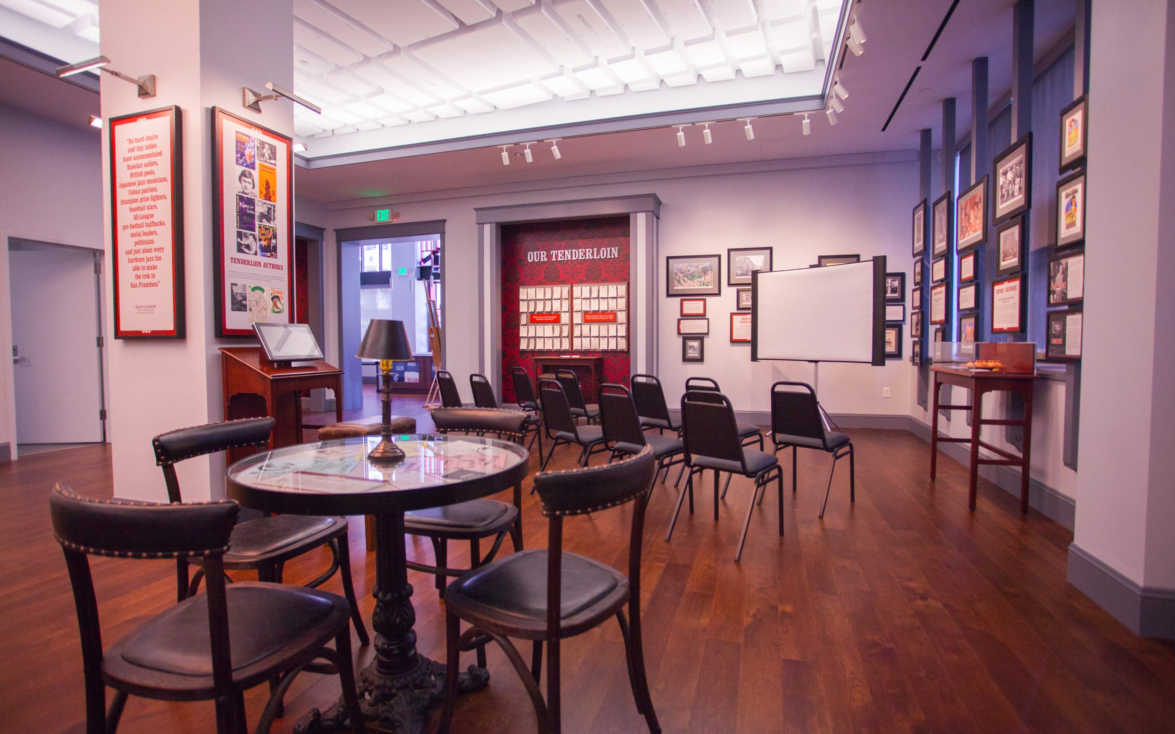 A brightly lit room with several chairs arranged around a round table, surrounded by framed pictures and historical displays on the walls.