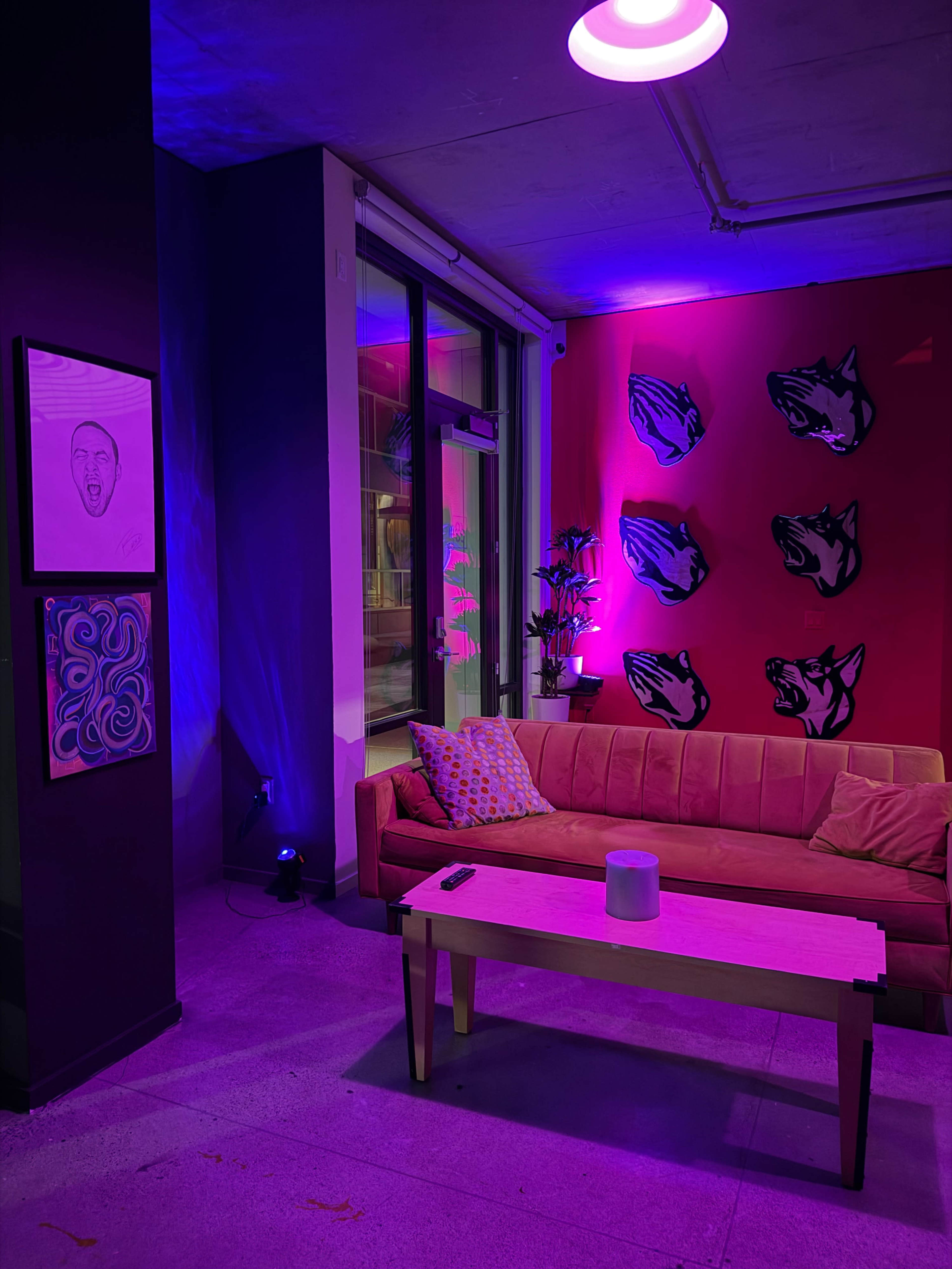 A vibrant lounge area features a pink-lit couch, a wooden coffee table, and artworks on the walls, with wolf head sculptures against a red backdrop.