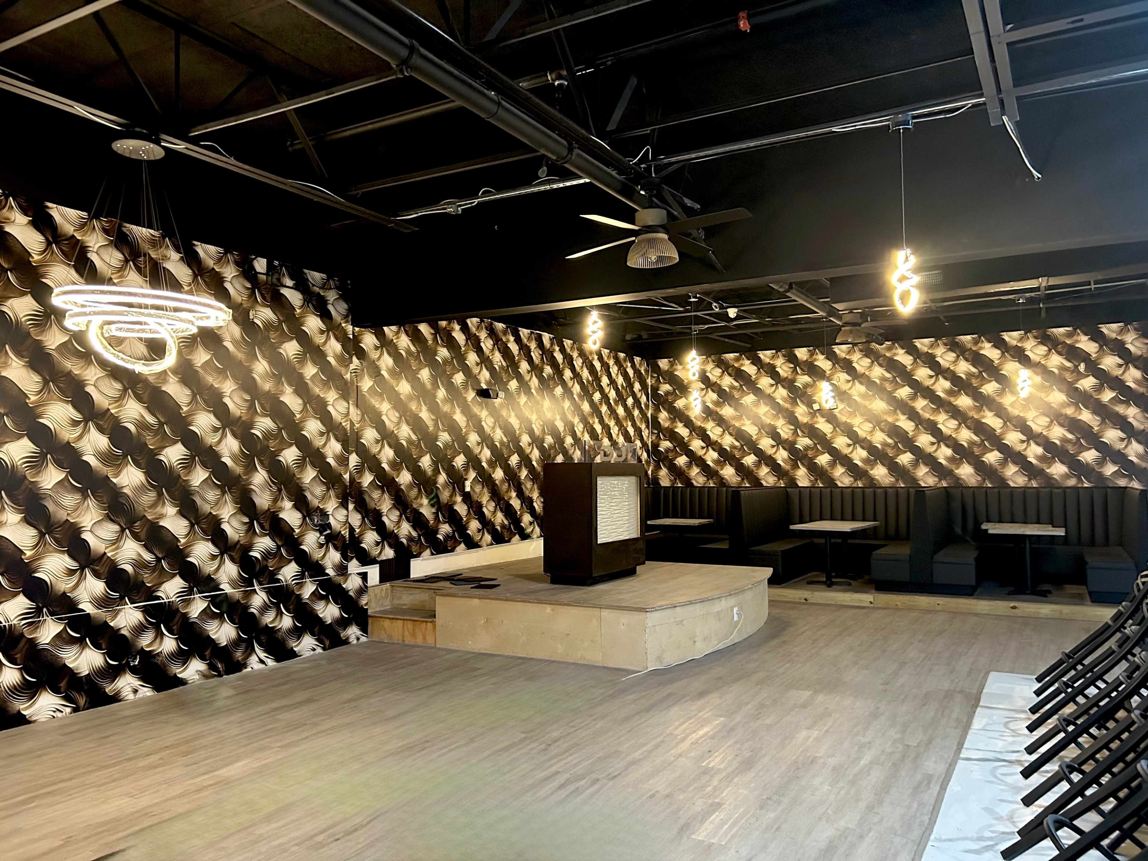 An empty interior space featuring patterned walls, a raised platform with a decorative panel, and seating areas with black booths.