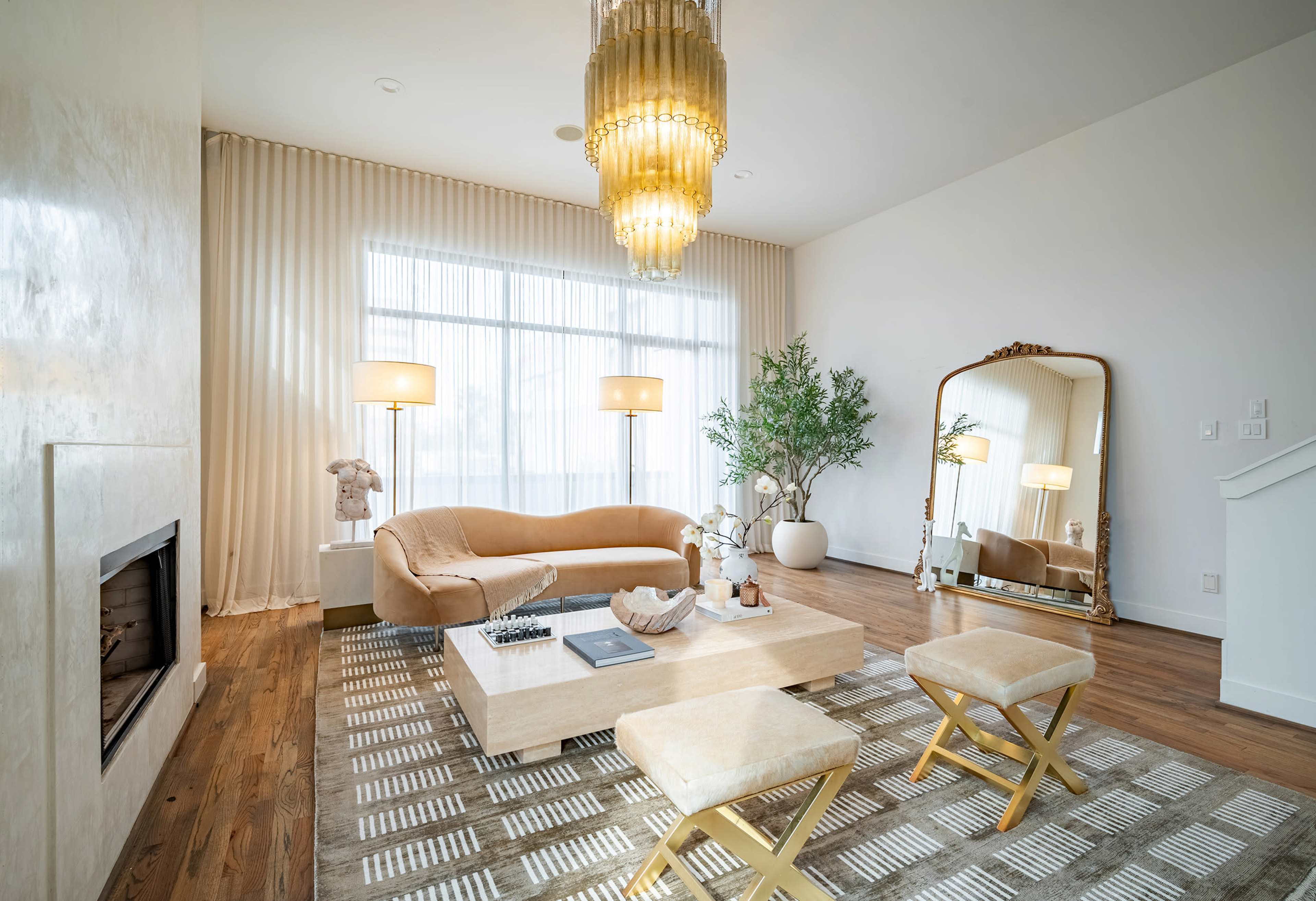 The living room features a light-colored sofa, a coffee table, decorative plants, and a large mirror under a chandelier, with tall windows letting in natural light.