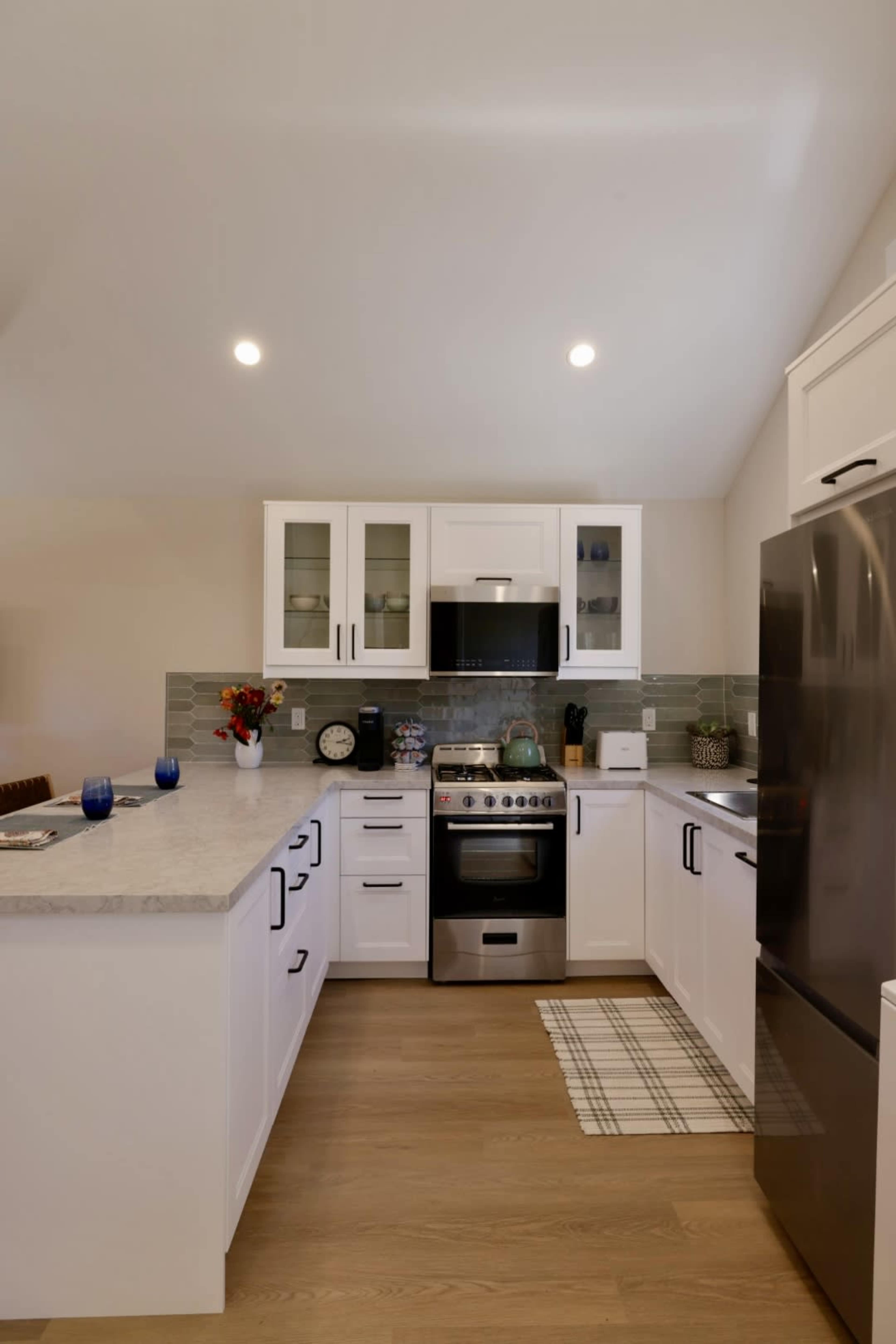 The kitchen features white cabinetry, stainless steel appliances, and a gray tile backsplash, with a decorative rug on the floor.