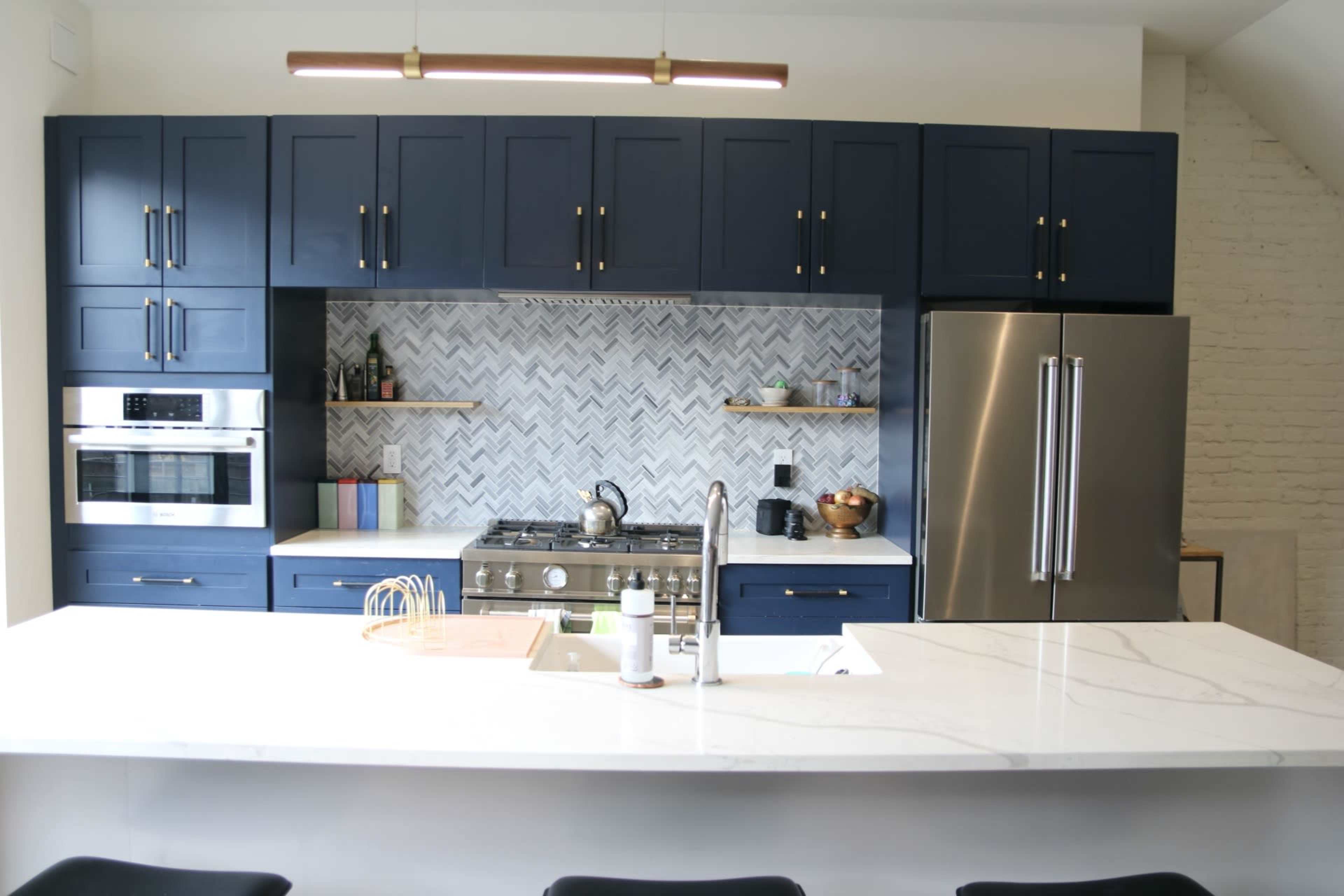 The image shows a modern kitchen featuring navy blue cabinets, a sleek marble countertop, and a herringbone-patterned backsplash.