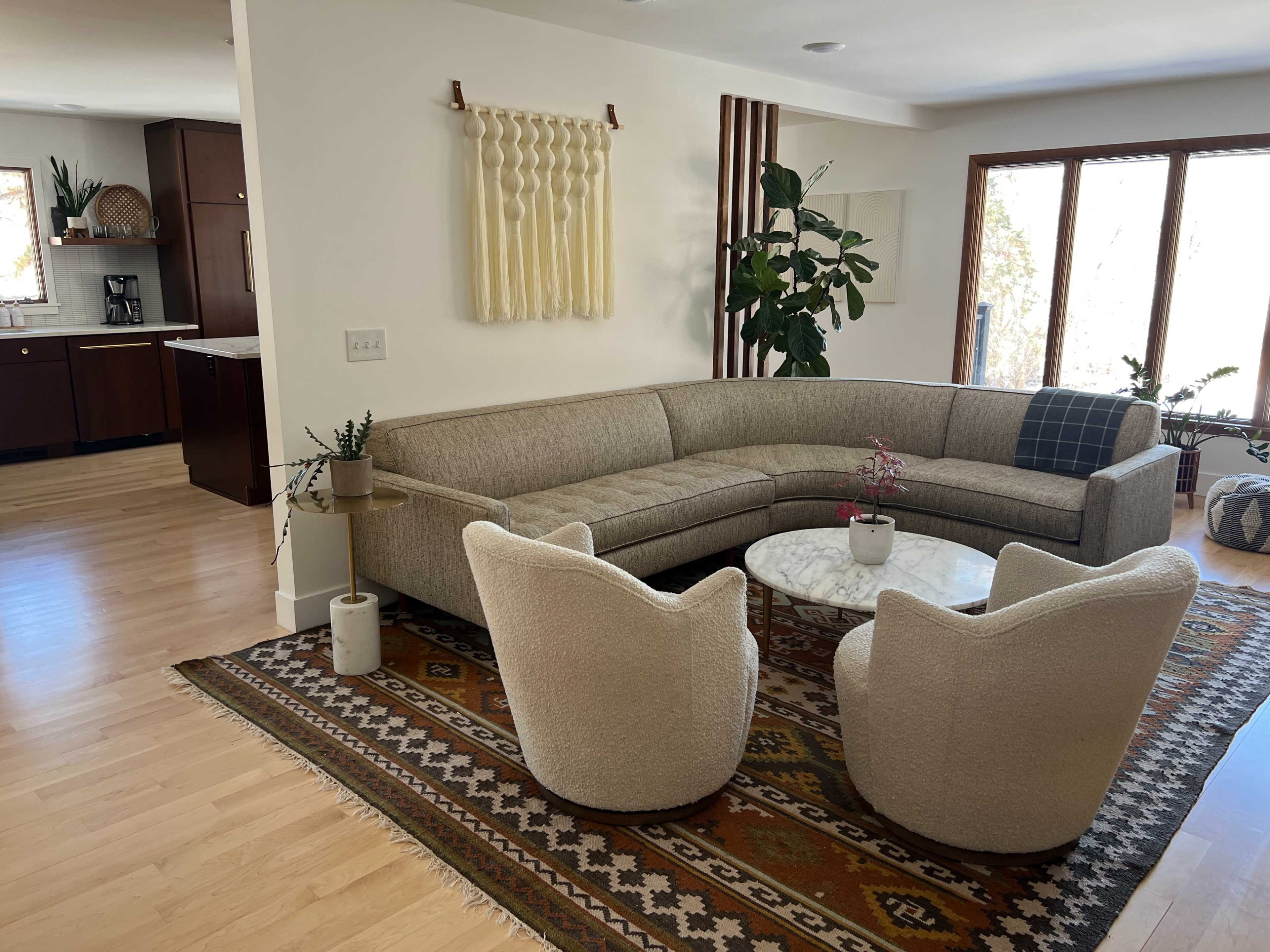 A modern living room with a curved beige sofa, two white armchairs, a round marble coffee table, and a patterned area rug.