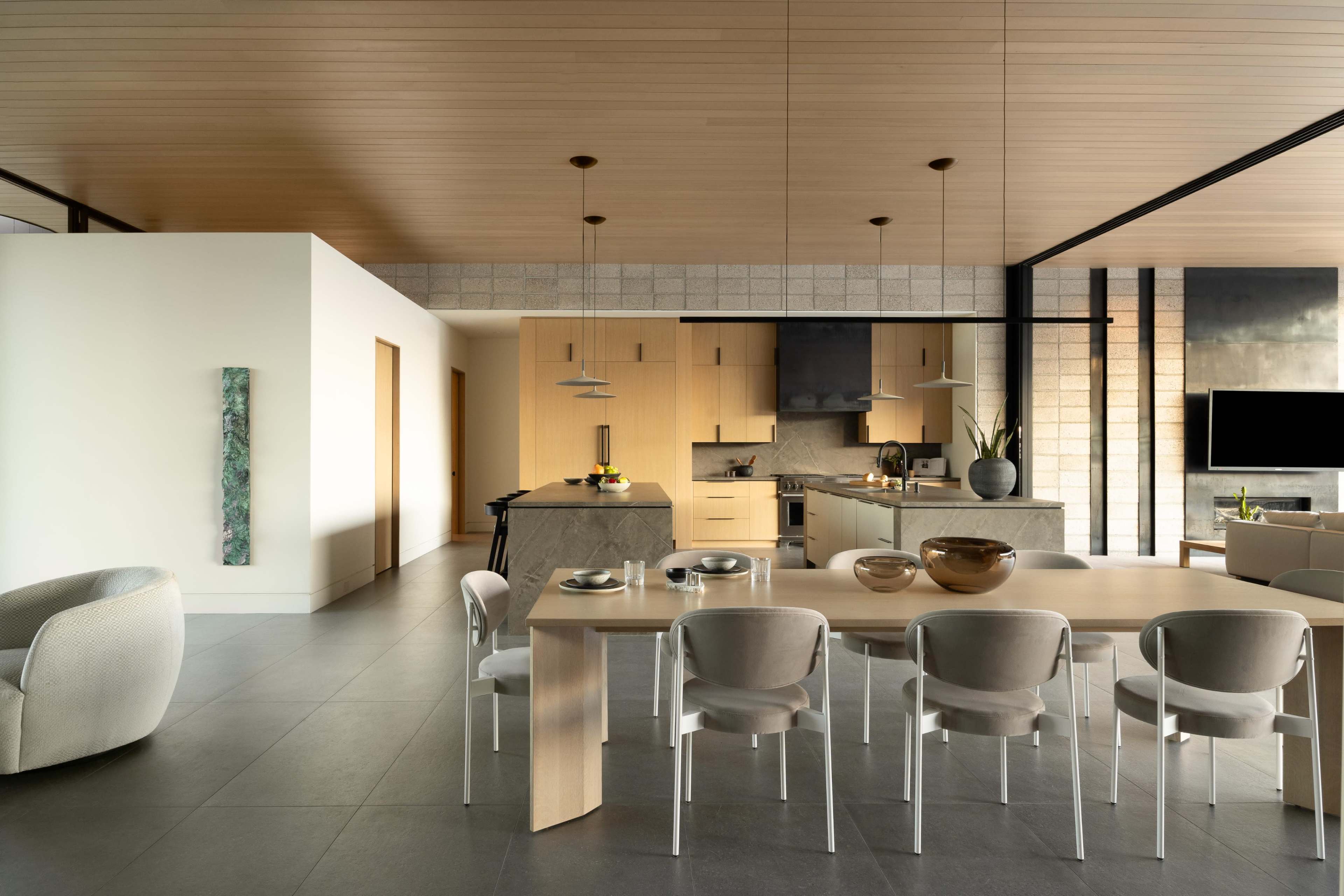 The image shows a modern kitchen and dining area featuring light wood cabinetry, a marble table, and minimalist furnishings.