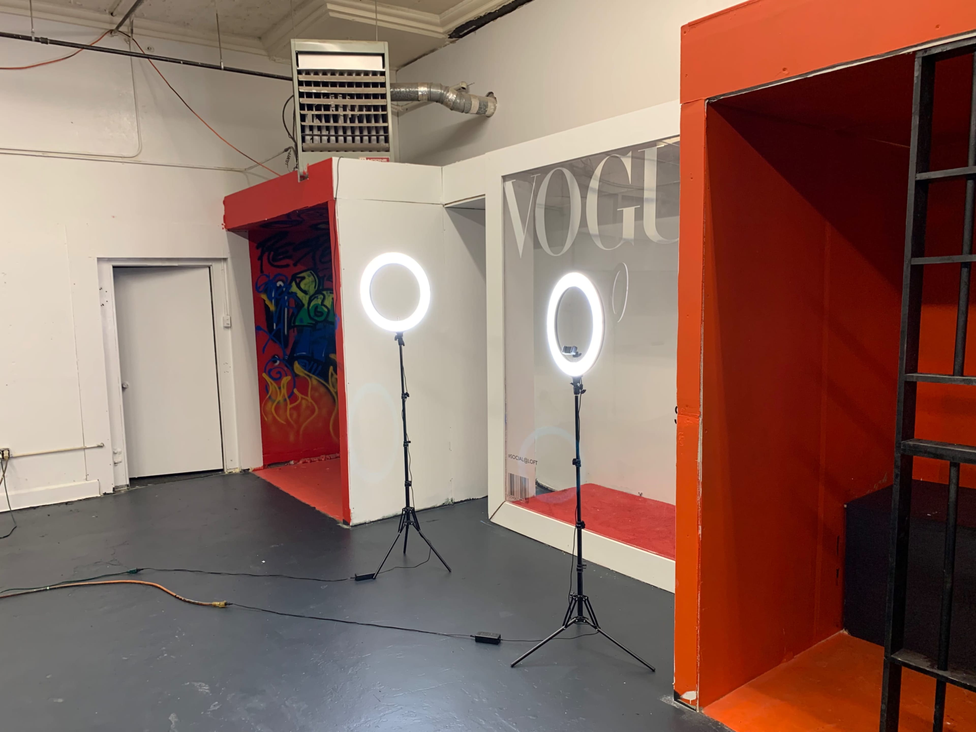 A studio space with two ring lights positioned near a brightly painted wall featuring a "VOGUE" display and a colorful mural.