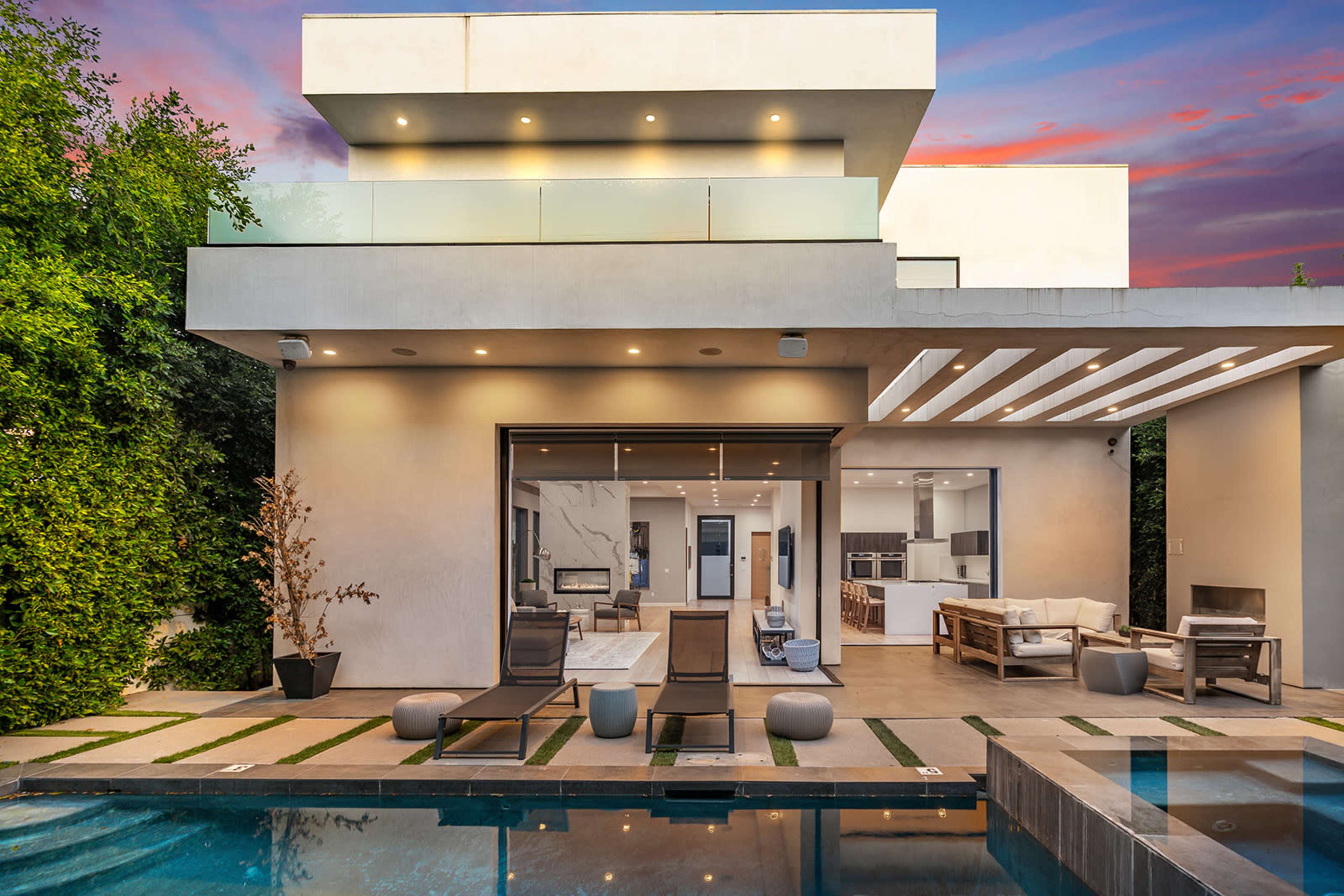 A modern two-story house features a swimming pool, outdoor seating area, and large glass doors opening to a spacious interior.