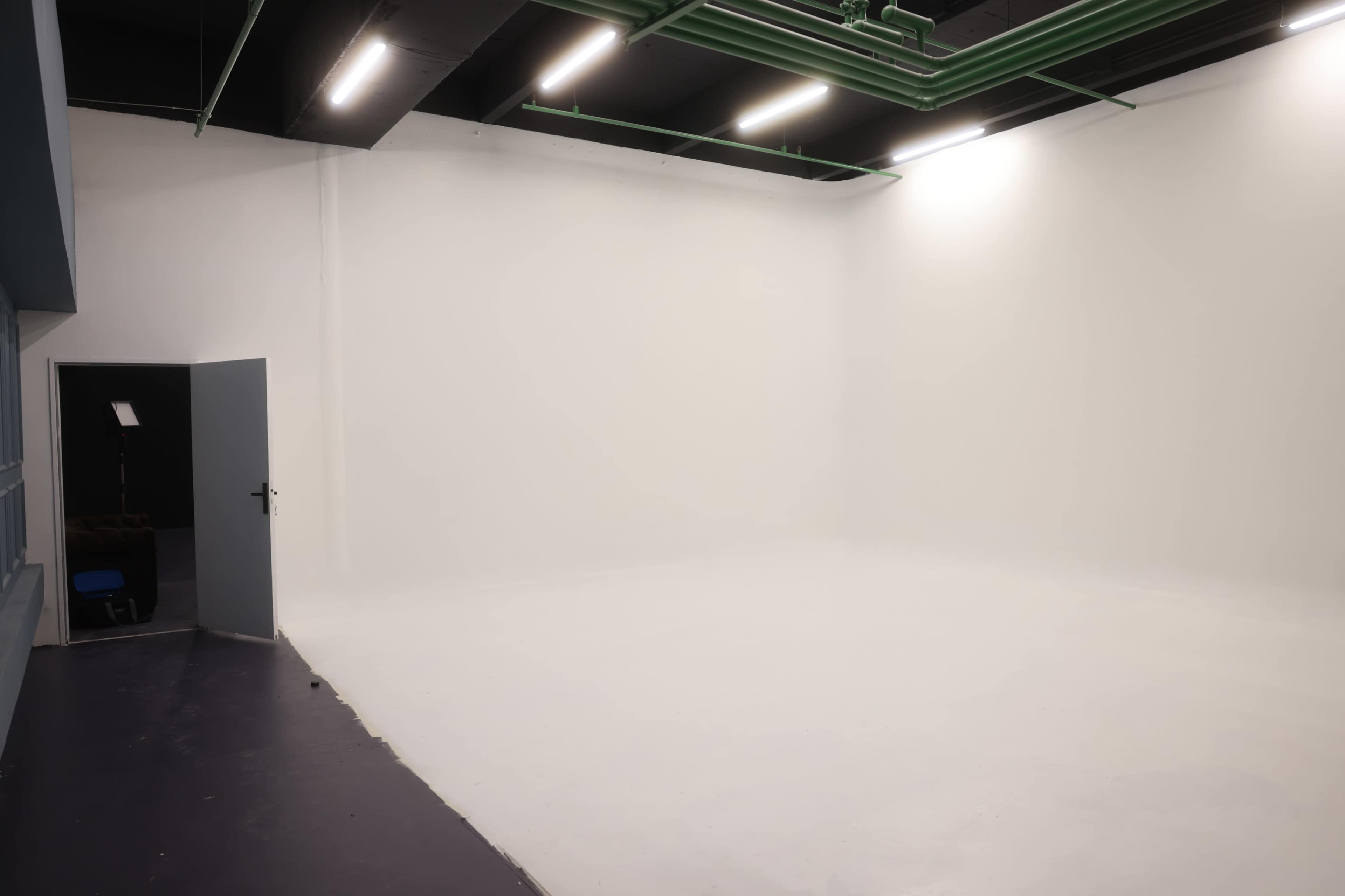 The image shows an empty, well-lit studio with white walls and a gray door on the left side.