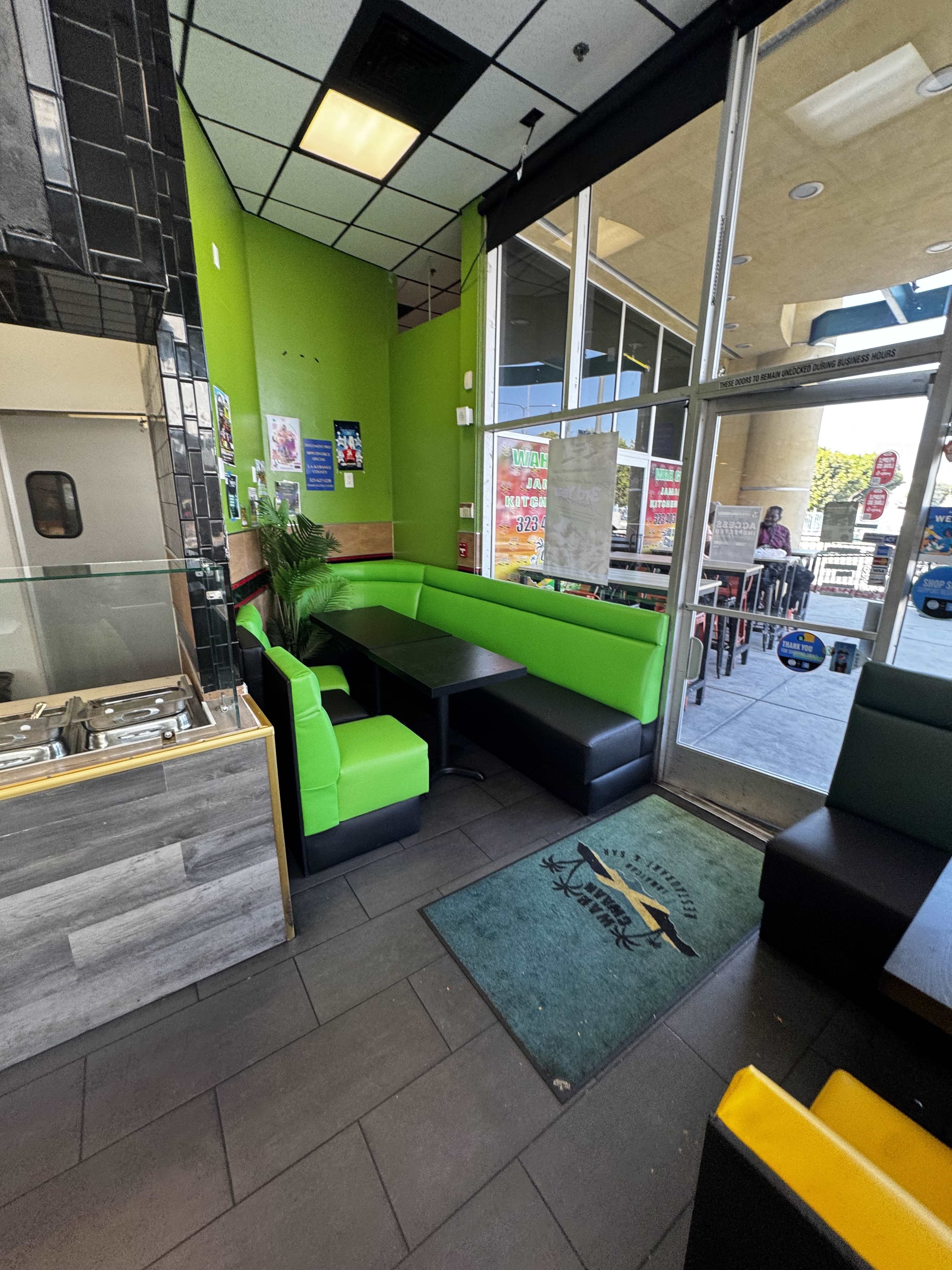 The image shows a brightly colored restaurant interior featuring a green and black seating area with a table, alongside an open entrance and visible outdoor seating.