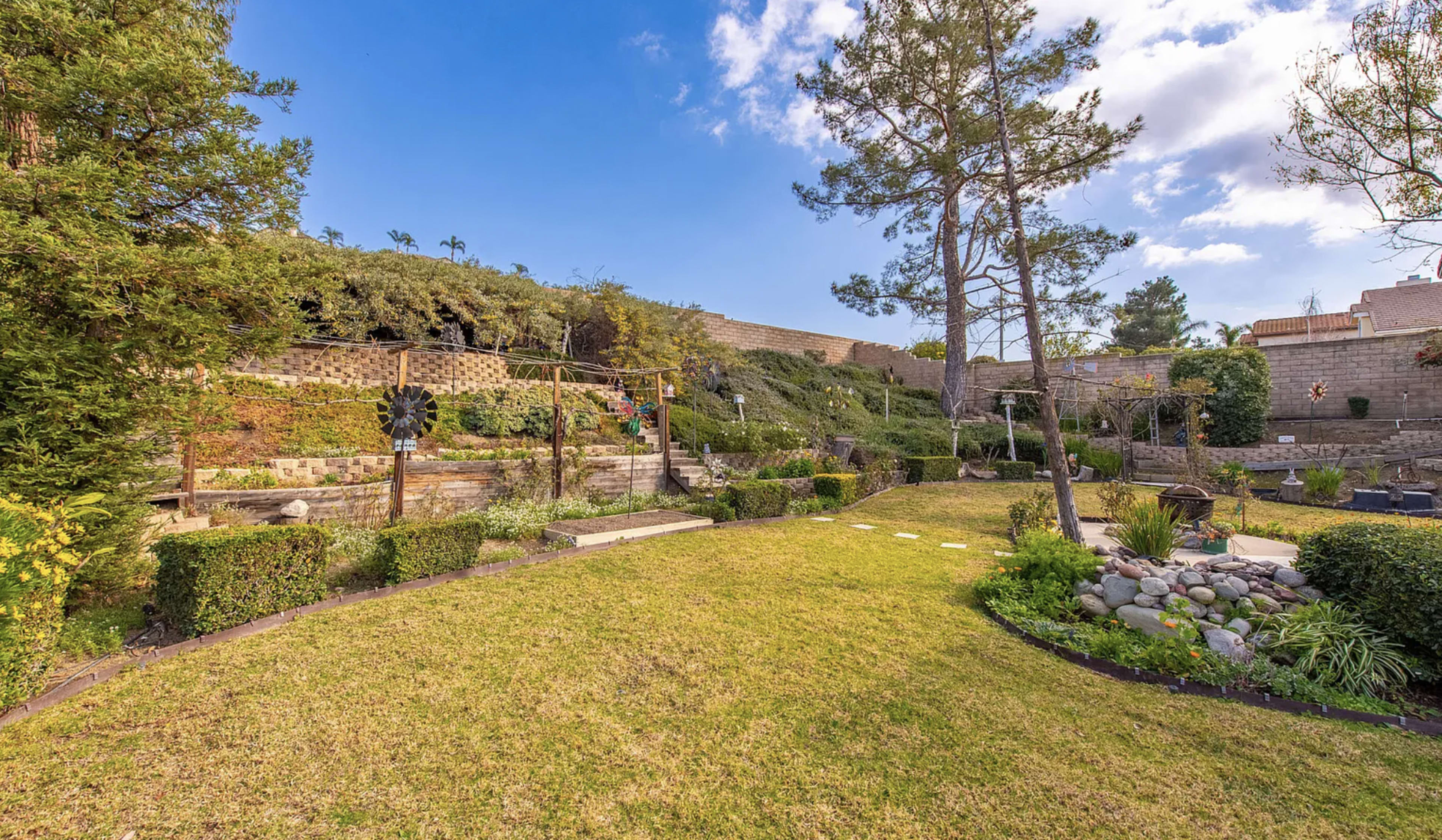 The image features a landscaped garden with neatly trimmed hedges, a stone wall in the background, and a decorative windmill.
