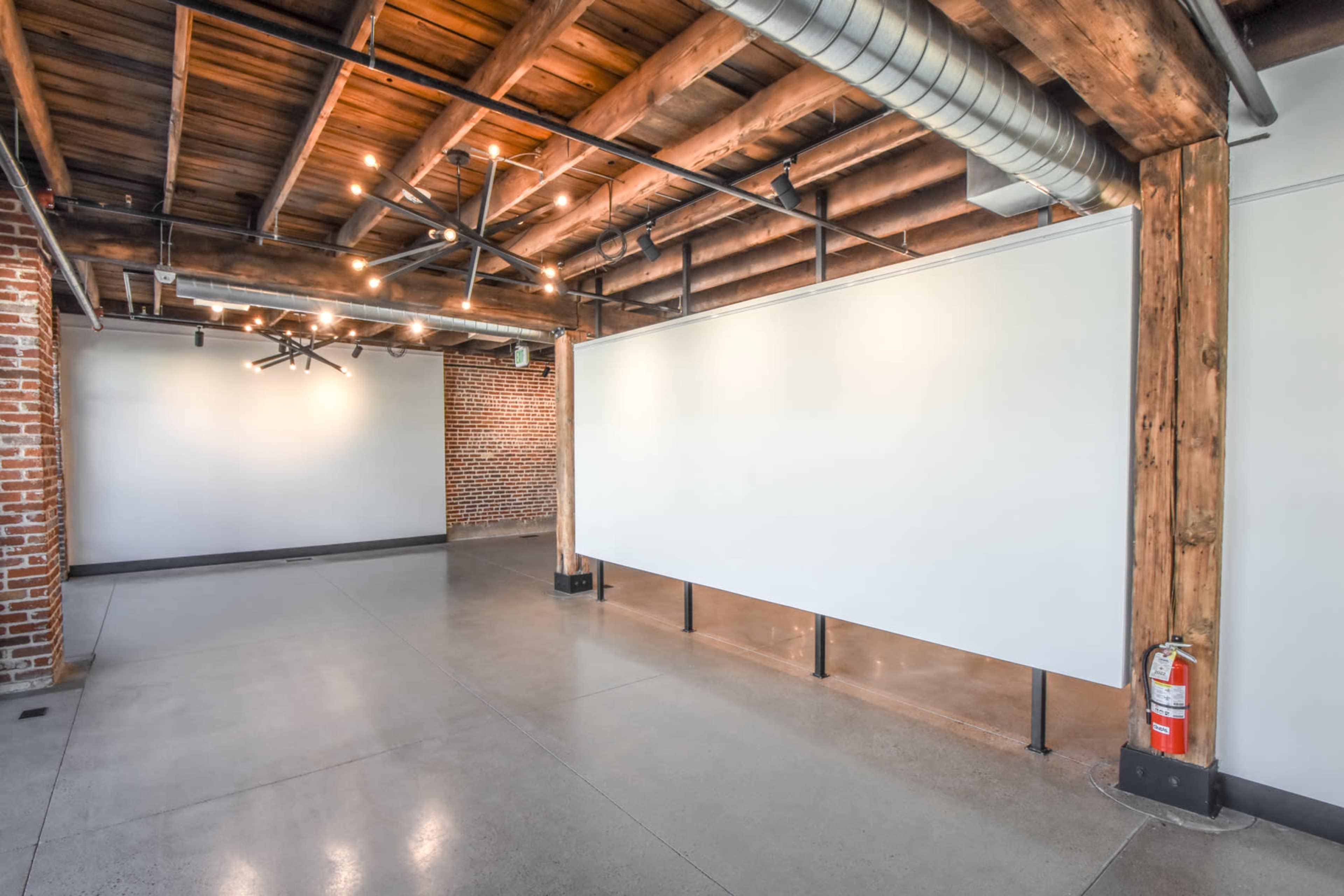 A spacious interior with exposed wooden beams, brick walls, and a clean, empty area featuring white panels and polished concrete floors.