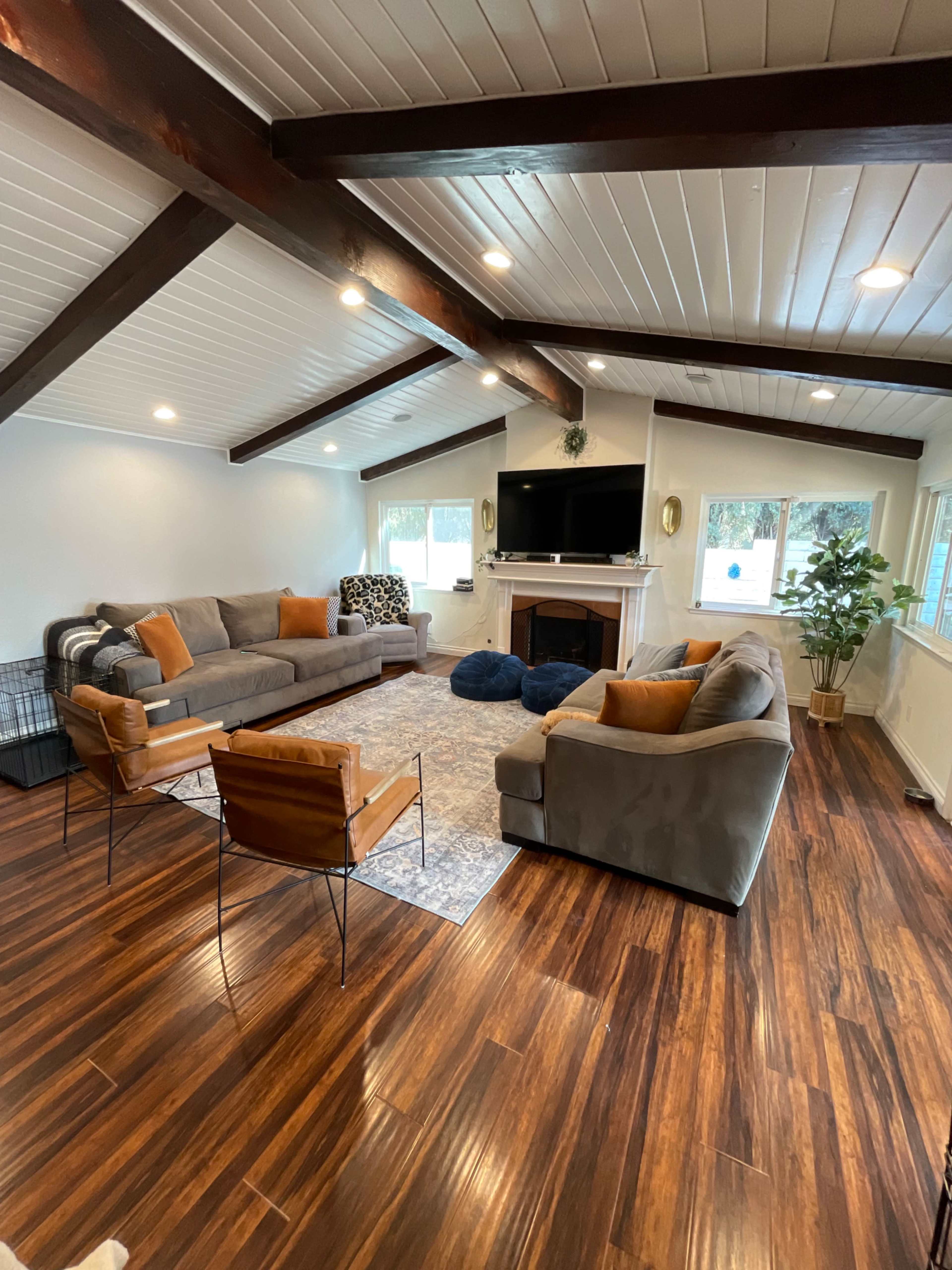 A spacious living room with a hardwood floor, featuring two sofas, a coffee table, a large rug, and a television above a fireplace.