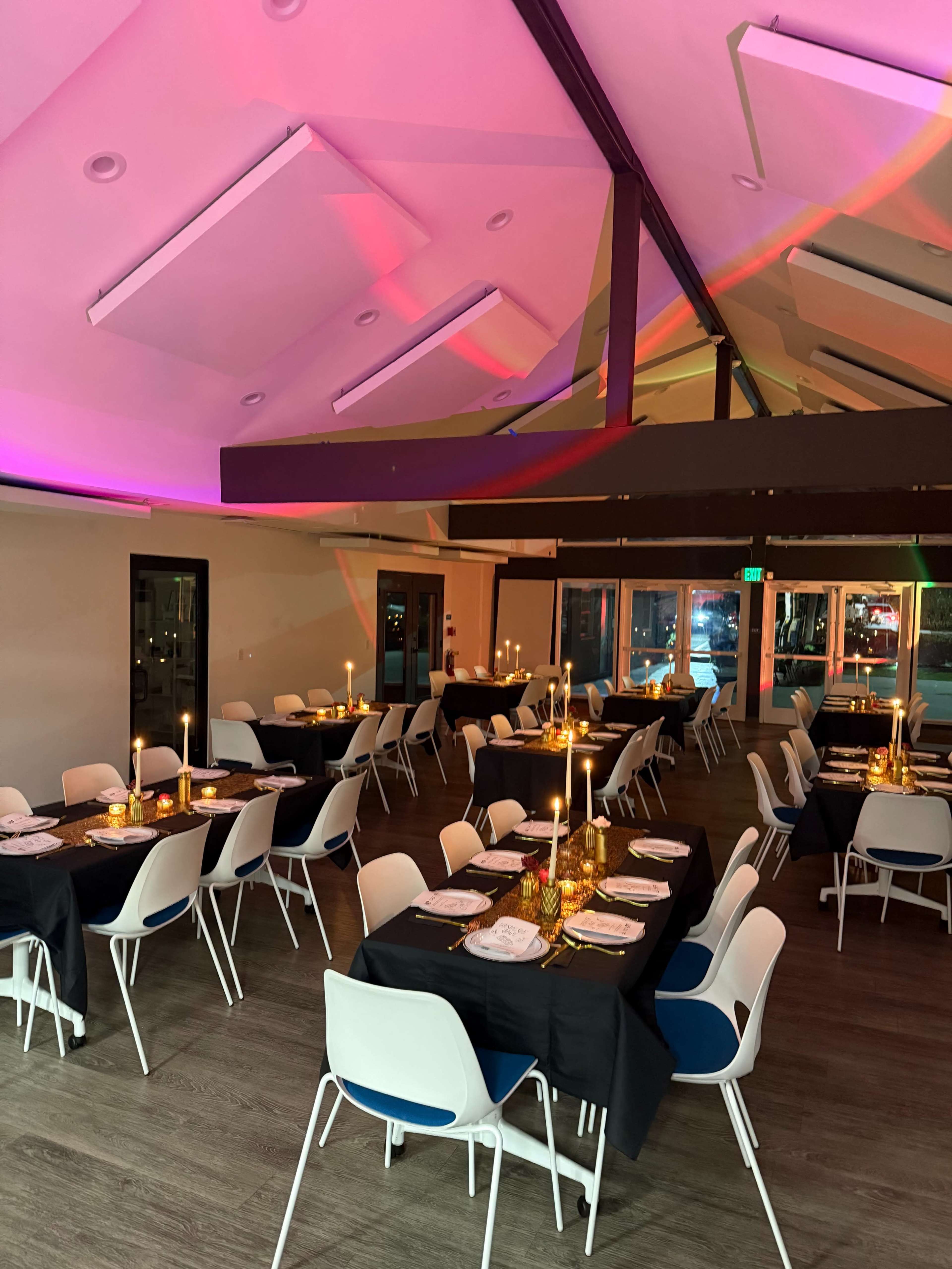 A well-arranged dining area features tables set with candles and elegant tableware under colorful lighting.