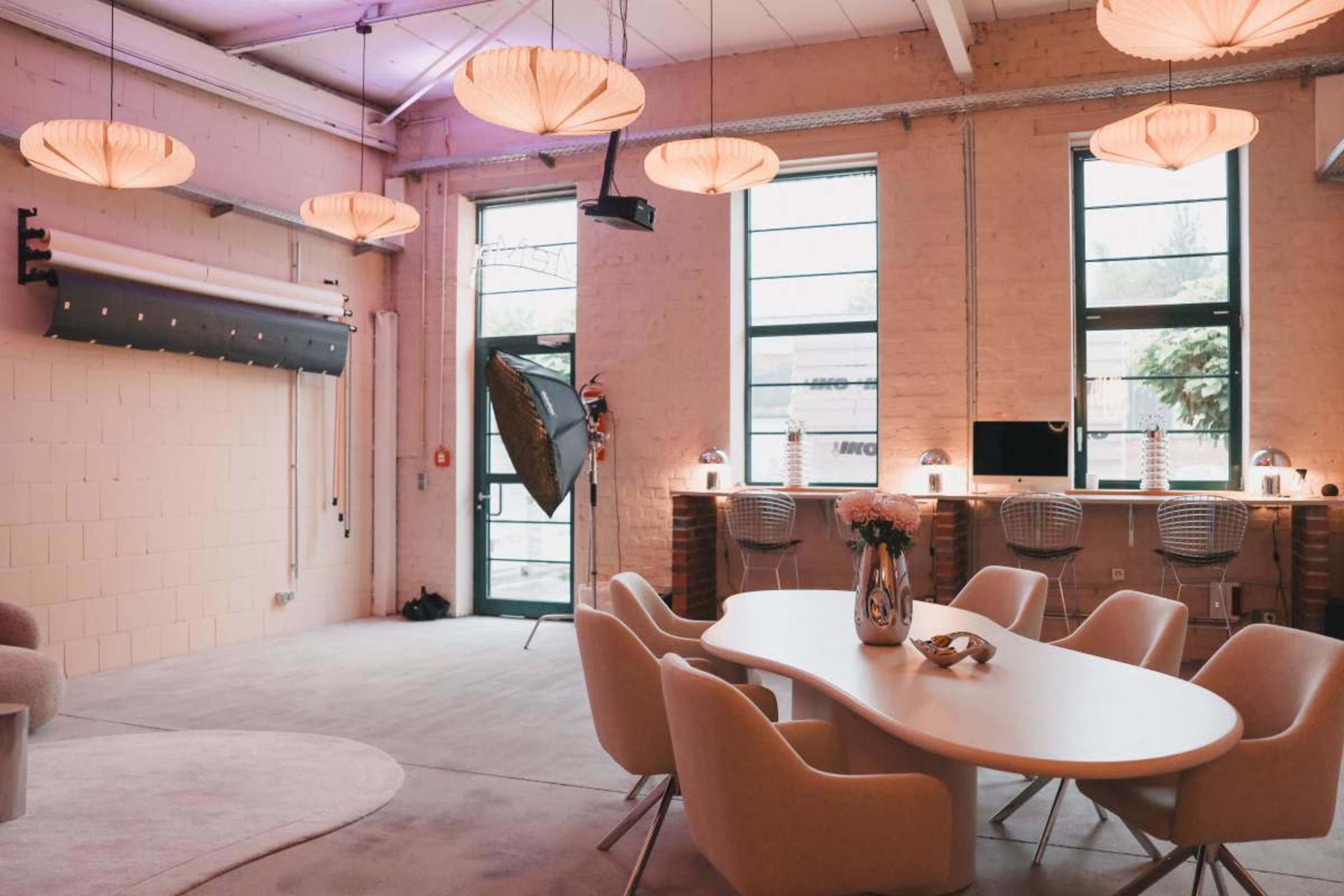 The image shows a modern, minimalist interior space with a round table surrounded by chairs, large windows, and pendant lighting.