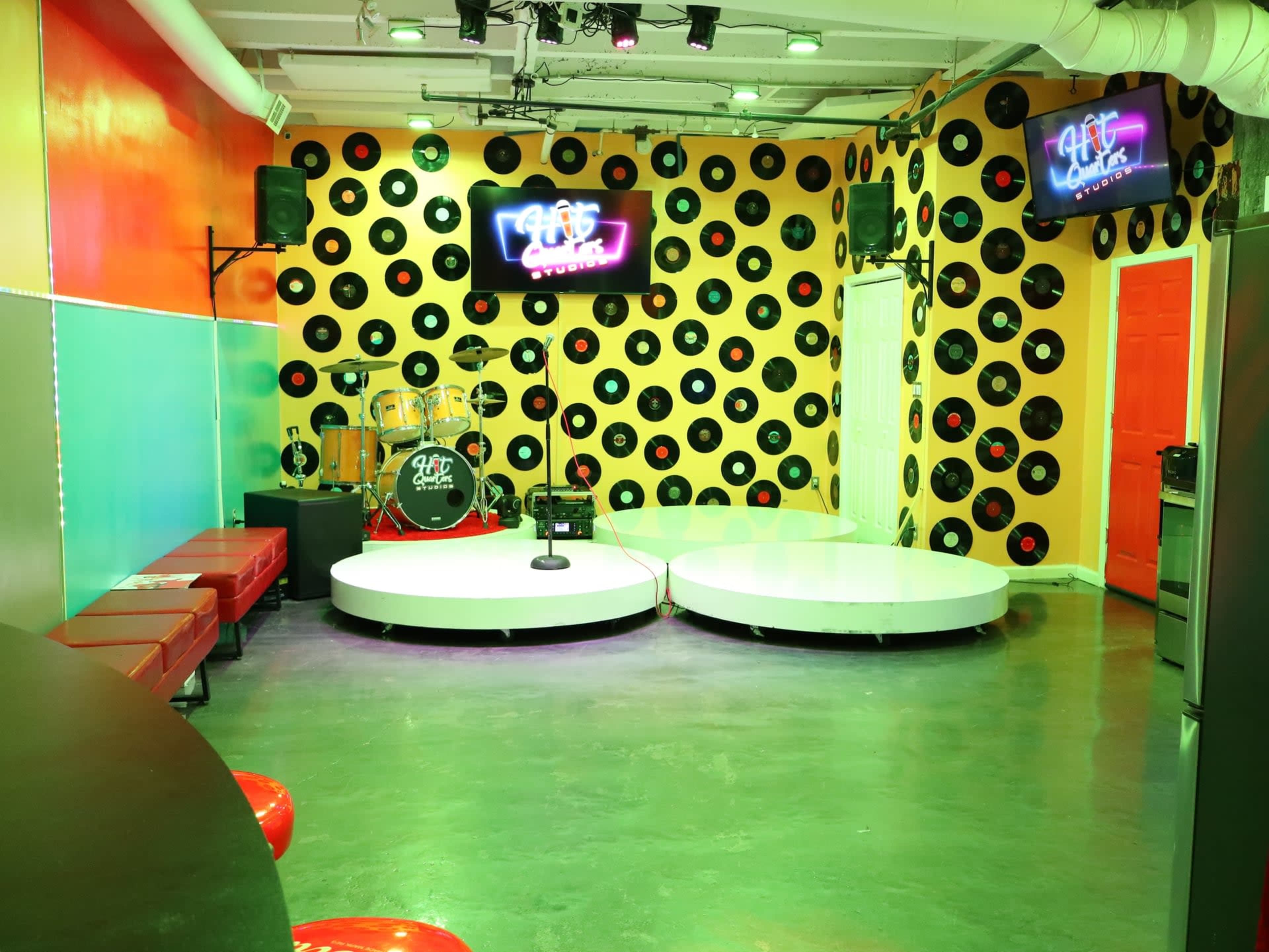 The image shows a vibrant music-themed room with a stage, seating area, and walls decorated with vinyl records.
