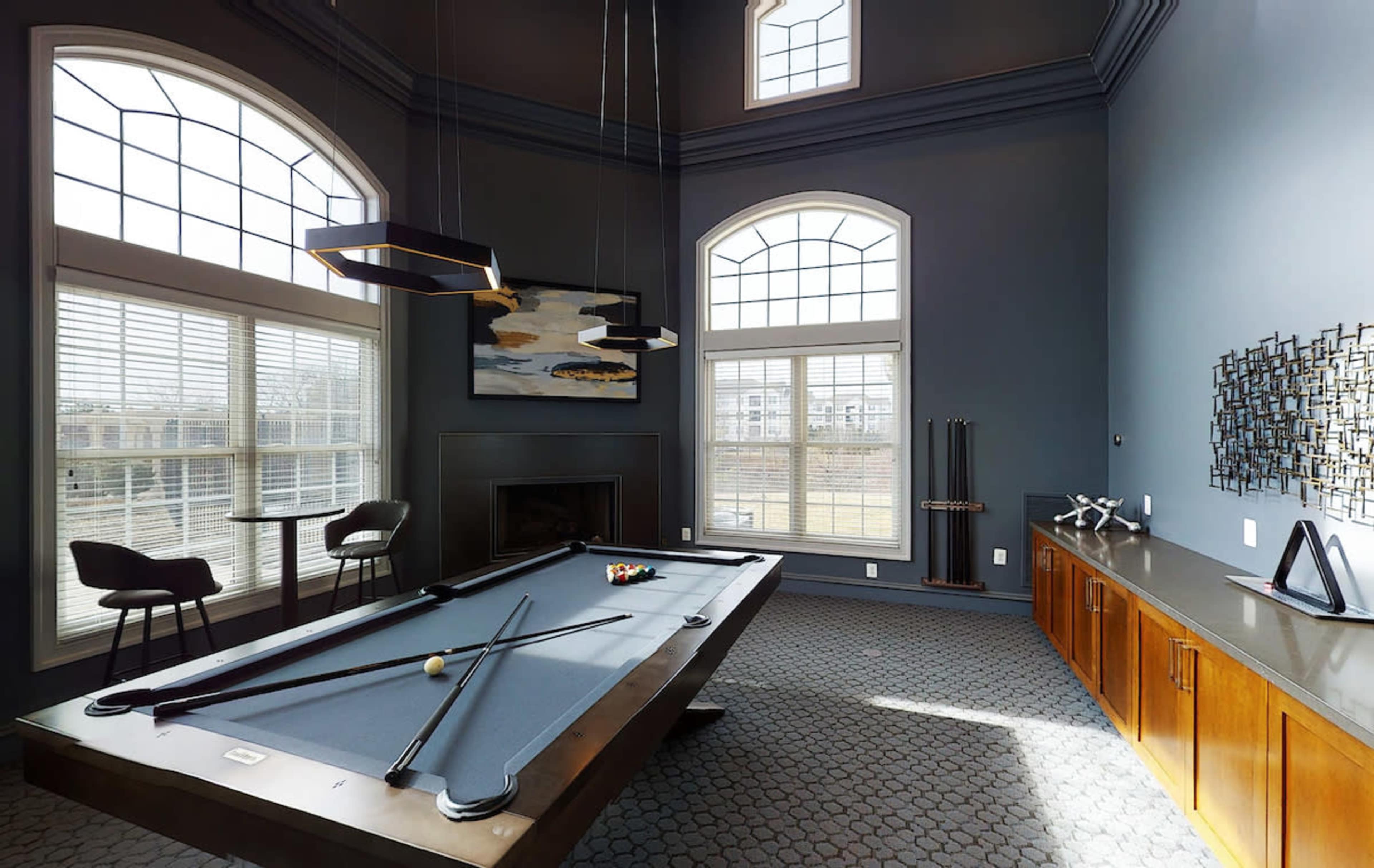 A spacious game room with a billiard table, tall windows, and modern furnishings.