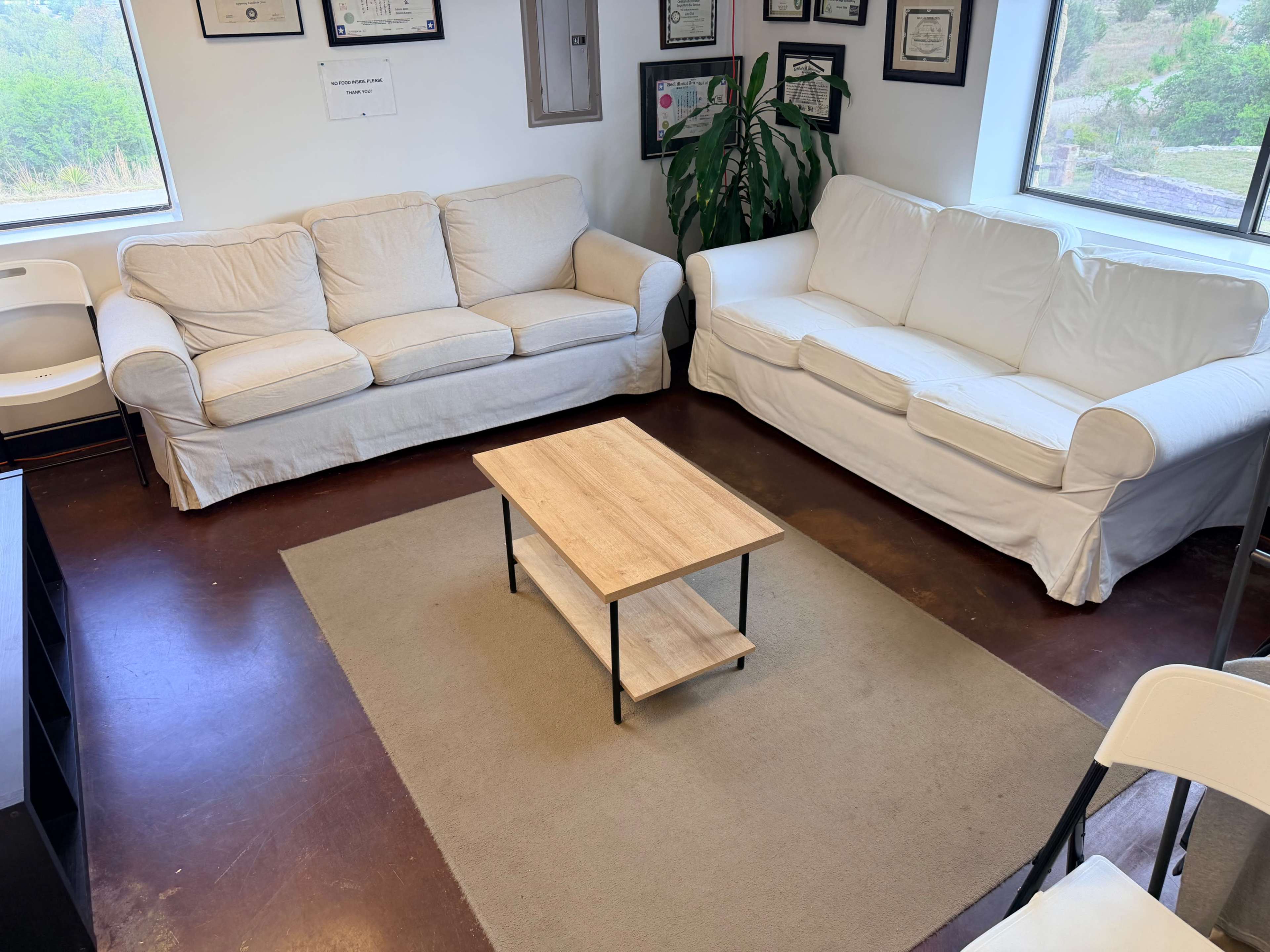 The image shows a room with two white sofas, a wooden coffee table, and a light-colored rug on a dark floor.