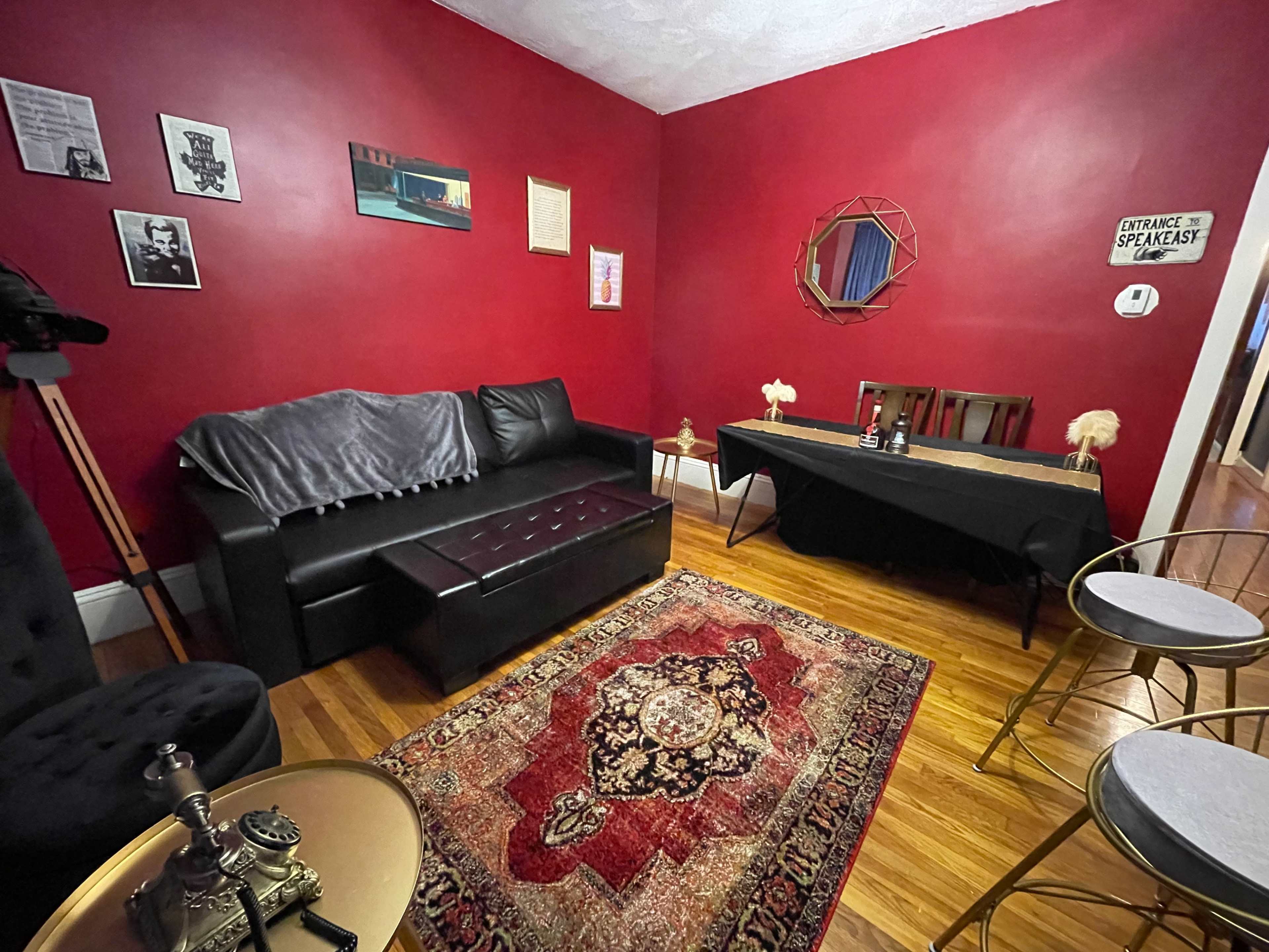 A living room with red walls, a black couch, a wooden dining table, and an ornate rug.