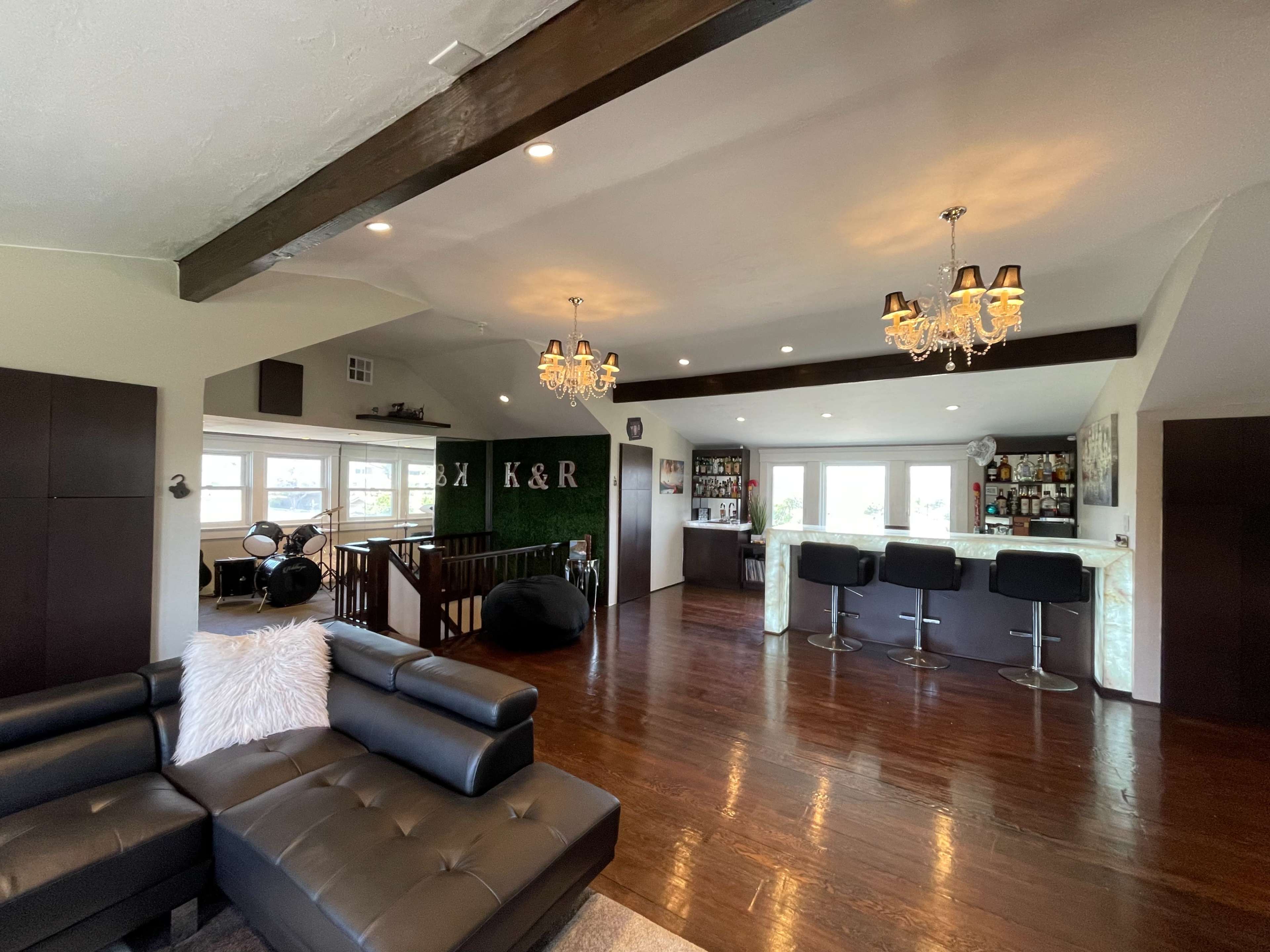 A modern living room with a black leather sectional sofa, hardwood floors, and a bar area featuring stools and a variety of bottles.