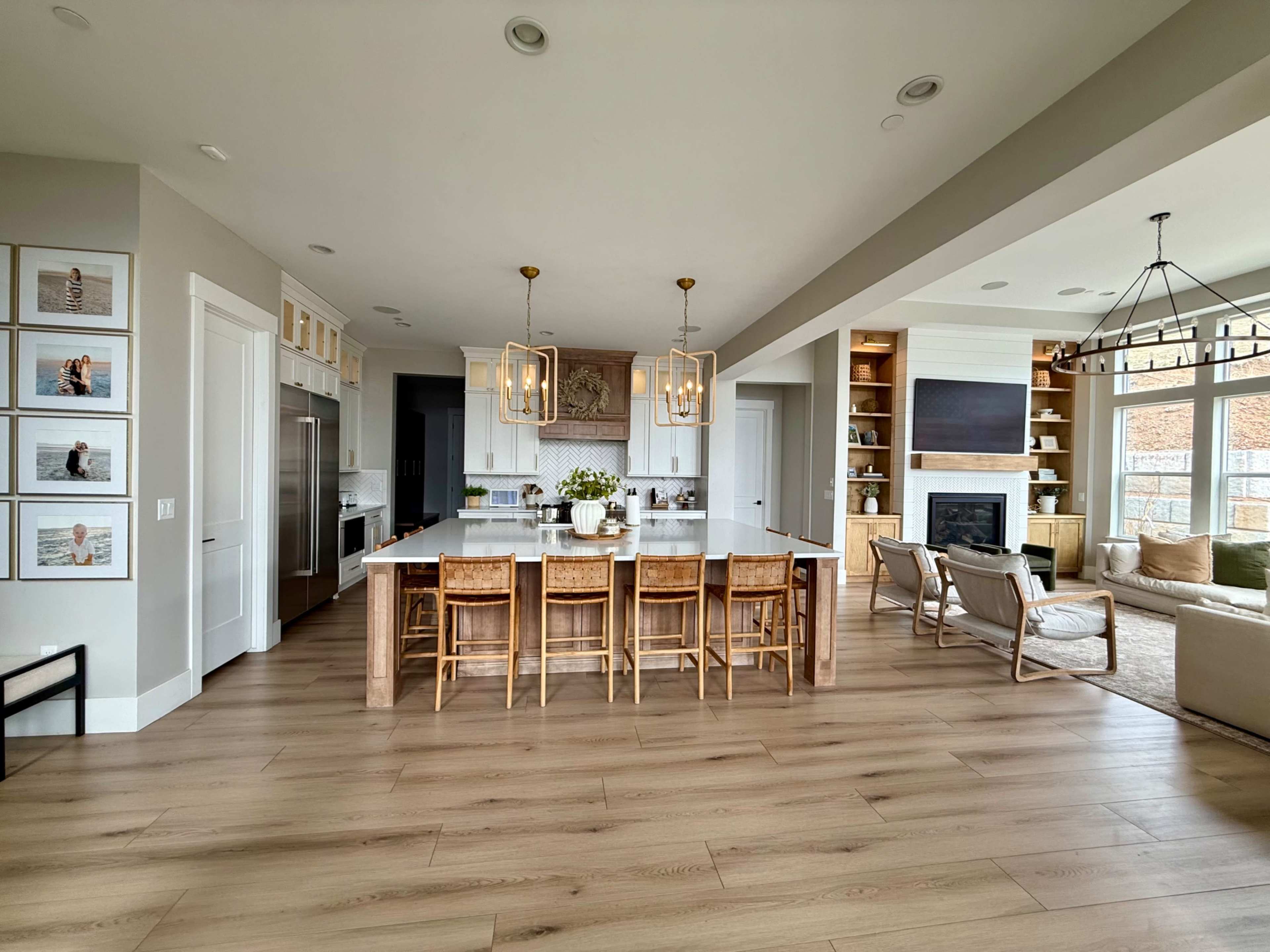 The image shows a modern kitchen and living area layout with a large island, bar seating, and a cozy seating arrangement near a fireplace.