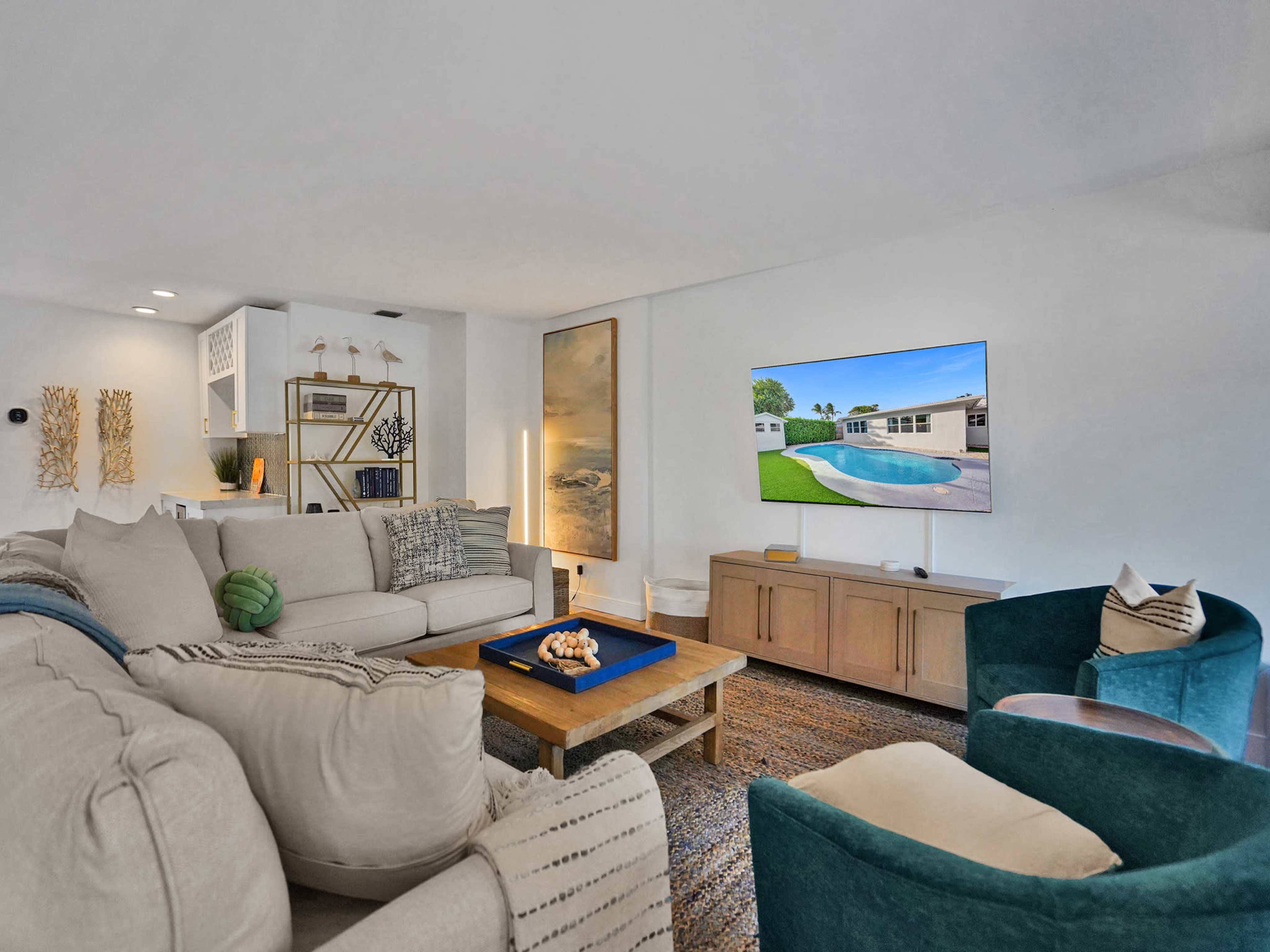 A modern living room featuring a large sectional sofa, an entertainment unit with a television displaying a pool view, and two armchairs, all arranged around a coffee table.