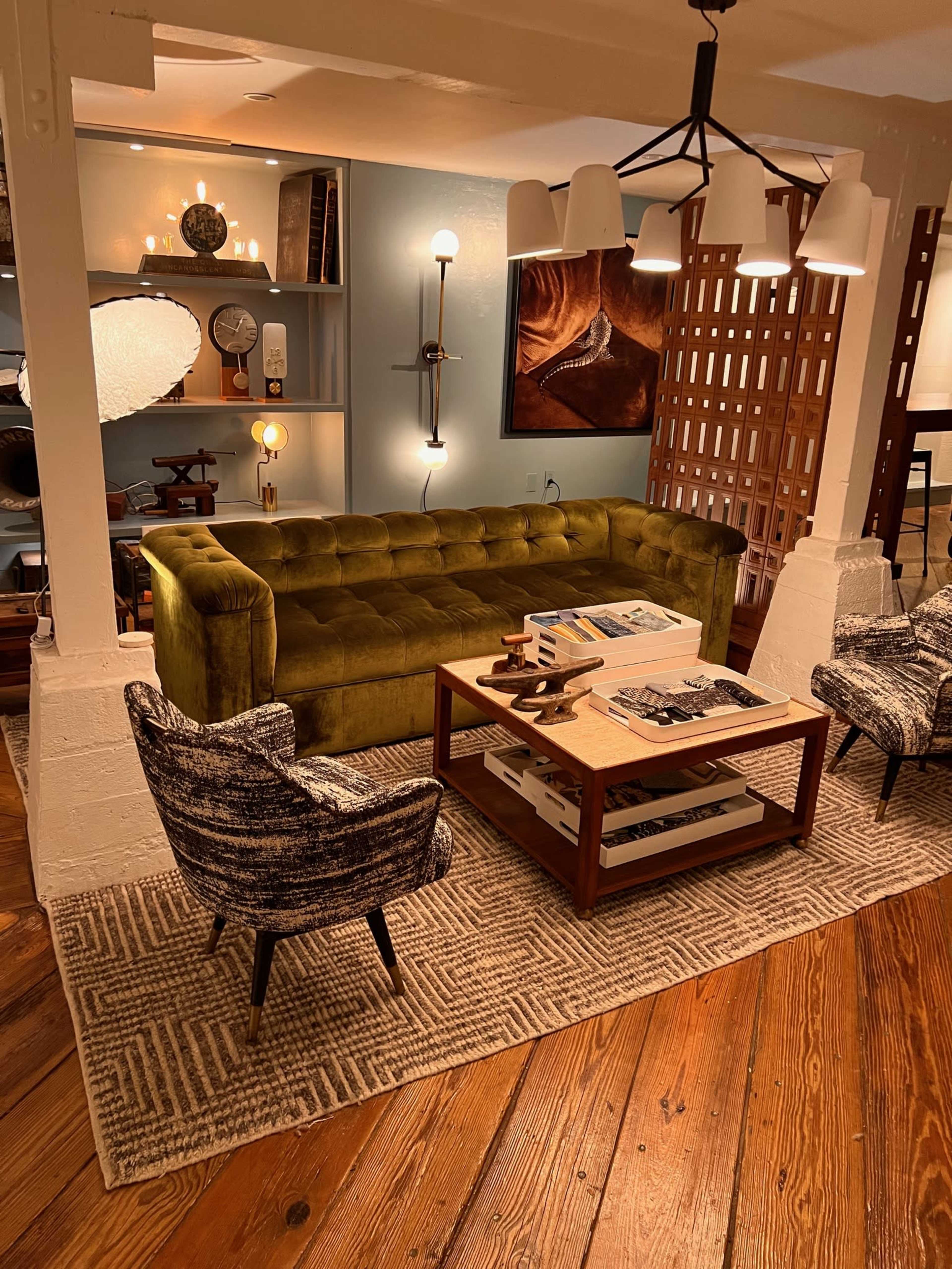 A cozy living room setup featuring a green tufted sofa, two patterned armchairs, a wooden coffee table with magazines, and a decorative rug on a wooden floor.