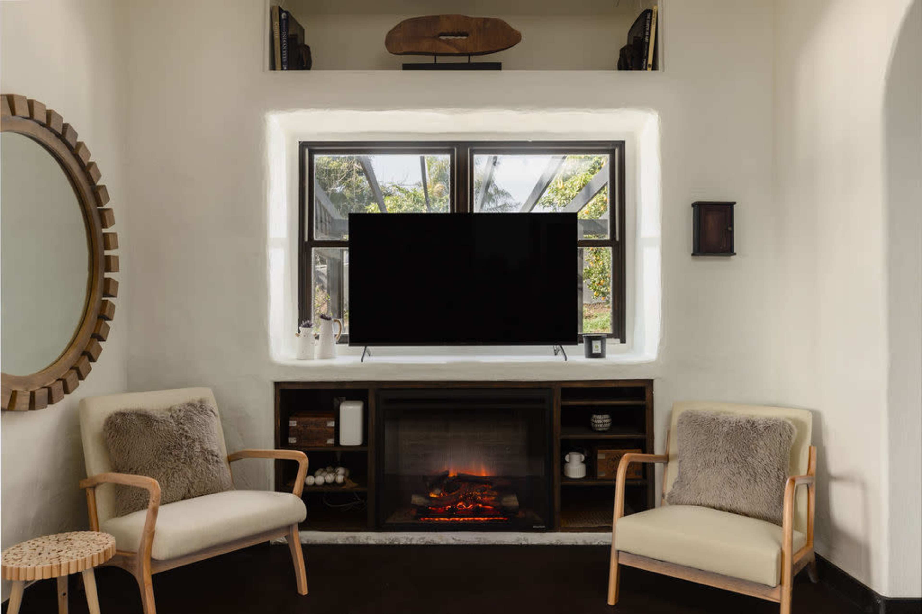A modern living room features two chairs facing a television above a fireplace, with natural light coming through a large window.