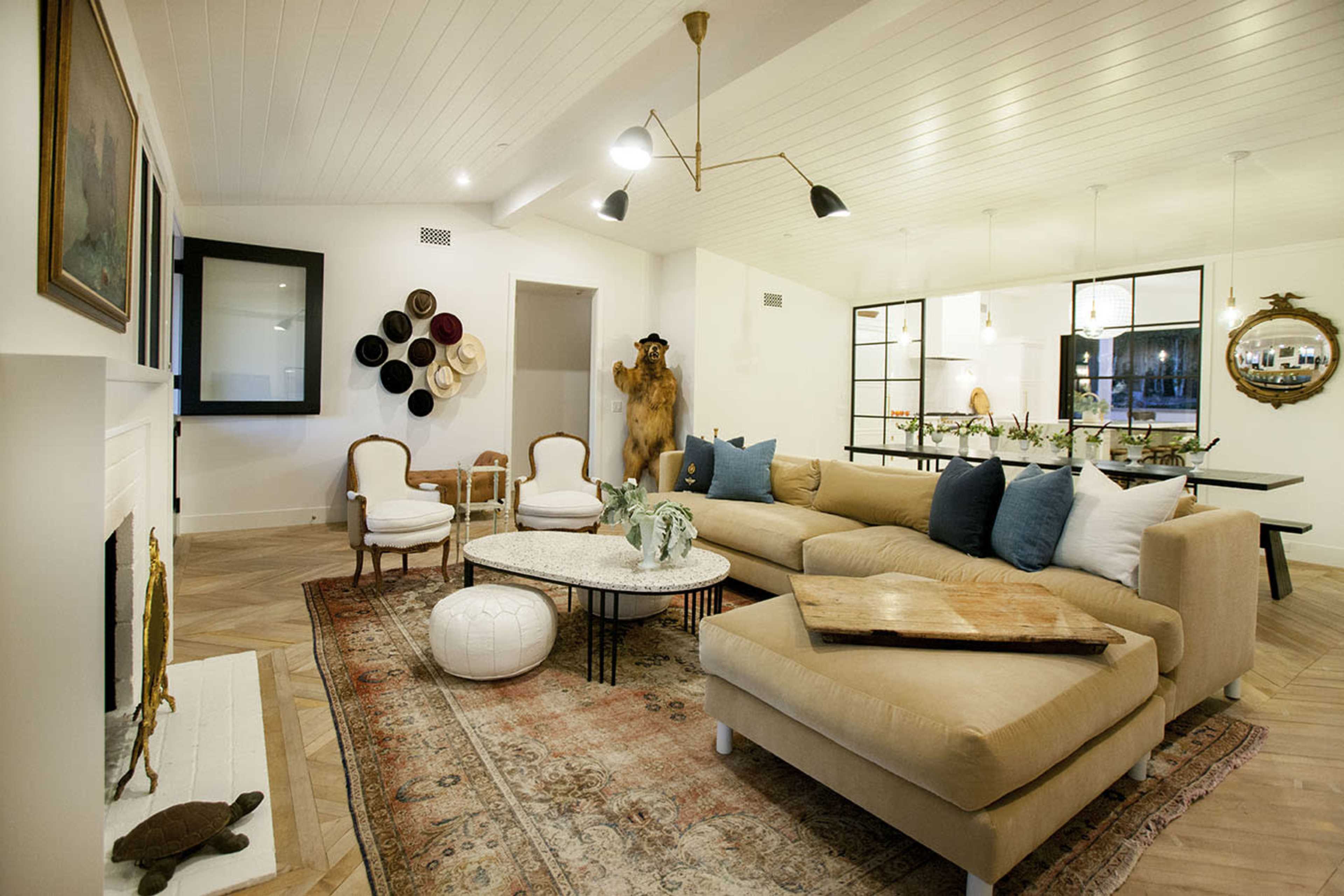 The living room features a large beige sectional couch, a coffee table, and decorative chairs arranged on a patterned rug beneath a paneled ceiling.