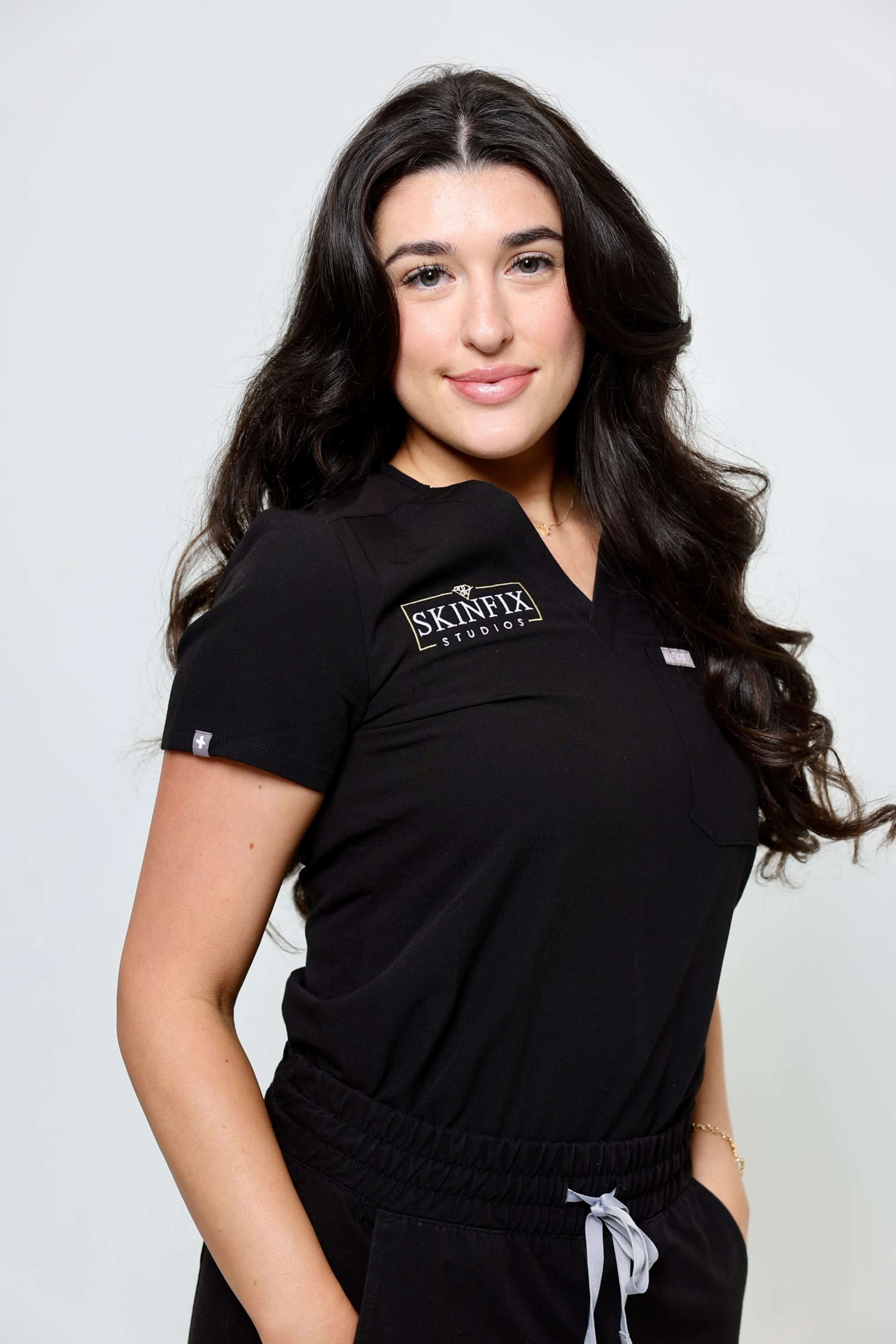 A person wearing a black uniform with a logo stands against a plain background, smiling at the camera.