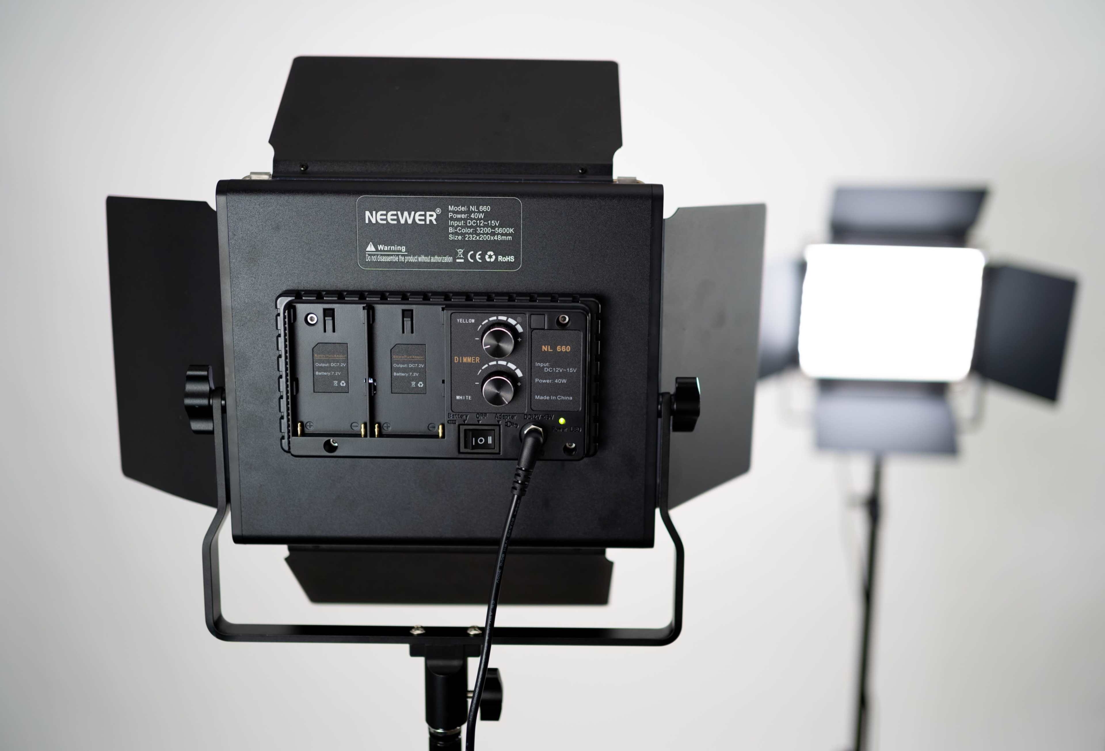 A Neewer lighting equipment setup with a control panel in focus and another light source blurred in the background.