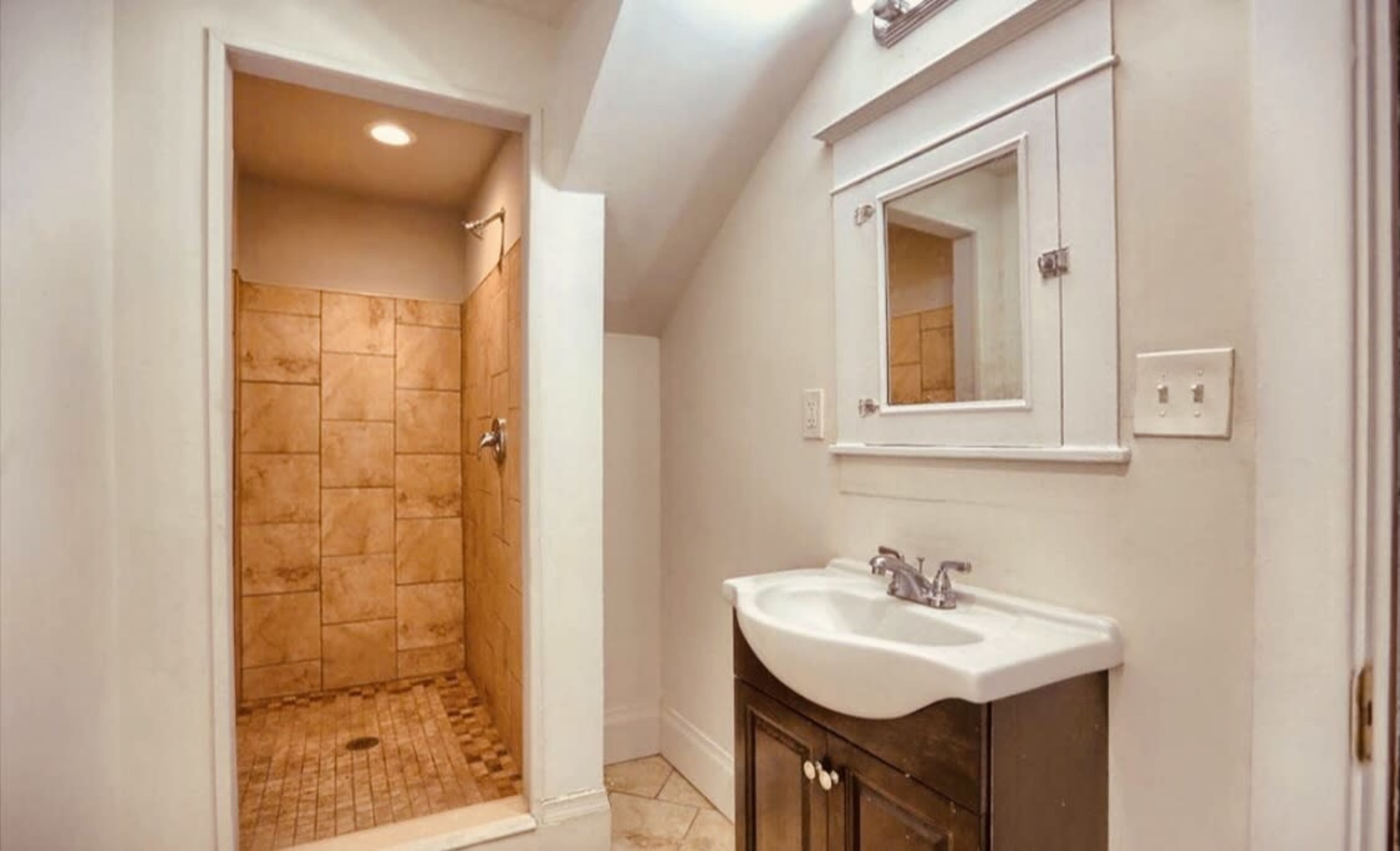 A small bathroom featuring a tiled shower area and a dark wood vanity with a sink and mirror.