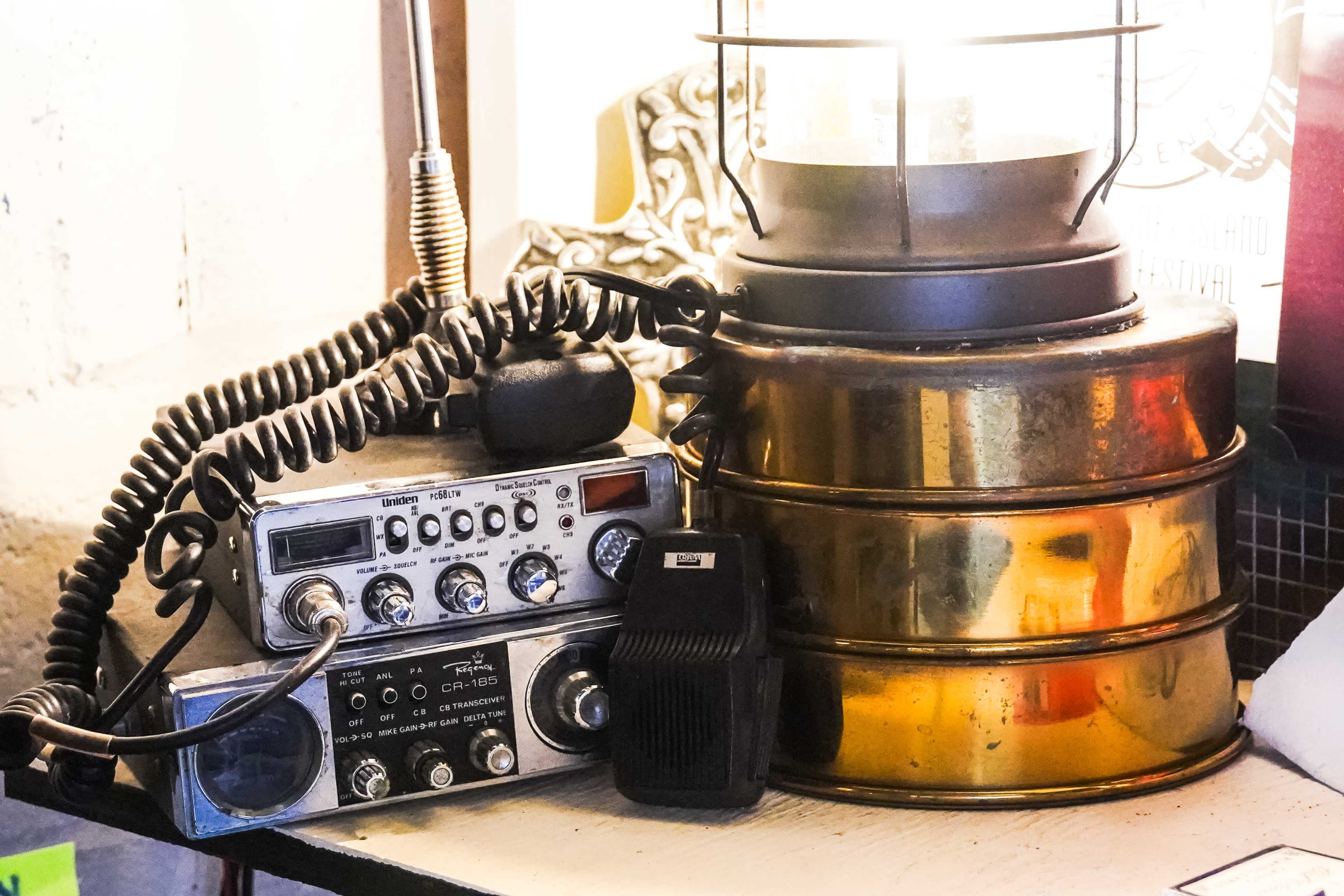 The image shows a vintage radio communication device stacked next to a brass lantern on a wooden table.
