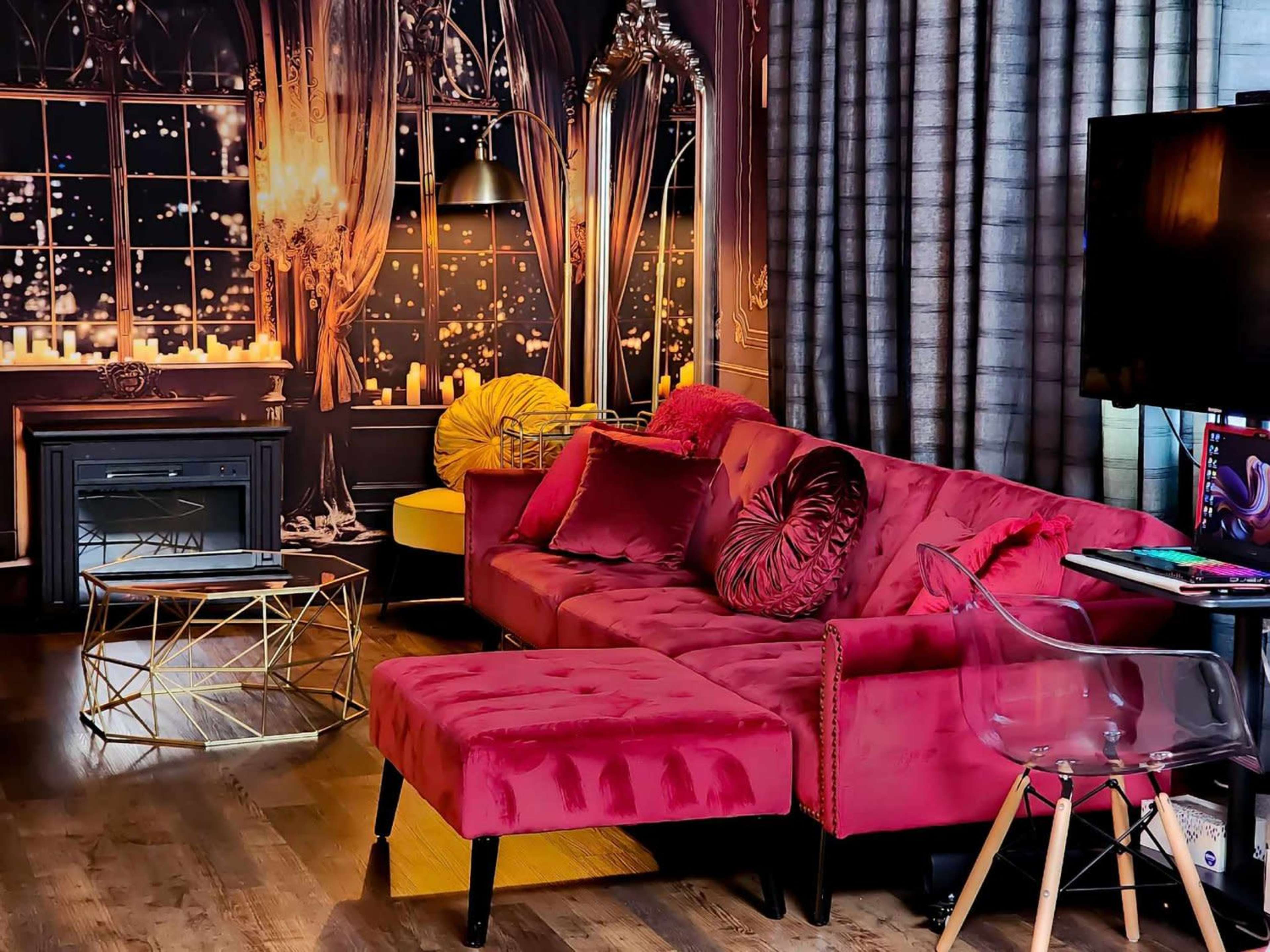 A lavish living room with a pink velvet sectional sofa, a glass coffee table, and a backdrop featuring a large window with city lights and candles.