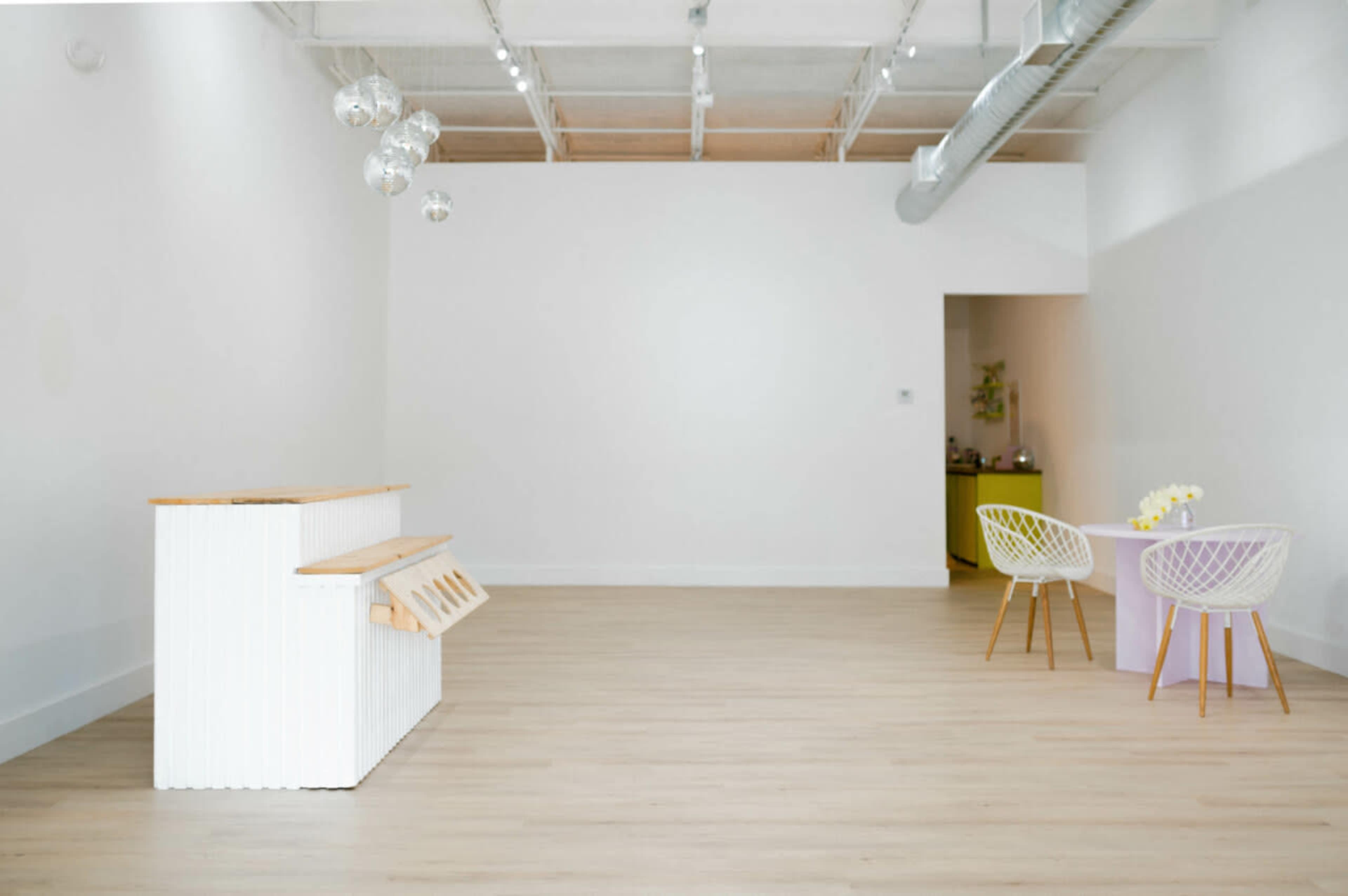 A spacious, minimally furnished interior with a white counter and two small tables, one with yellow and the other with purple accents.
