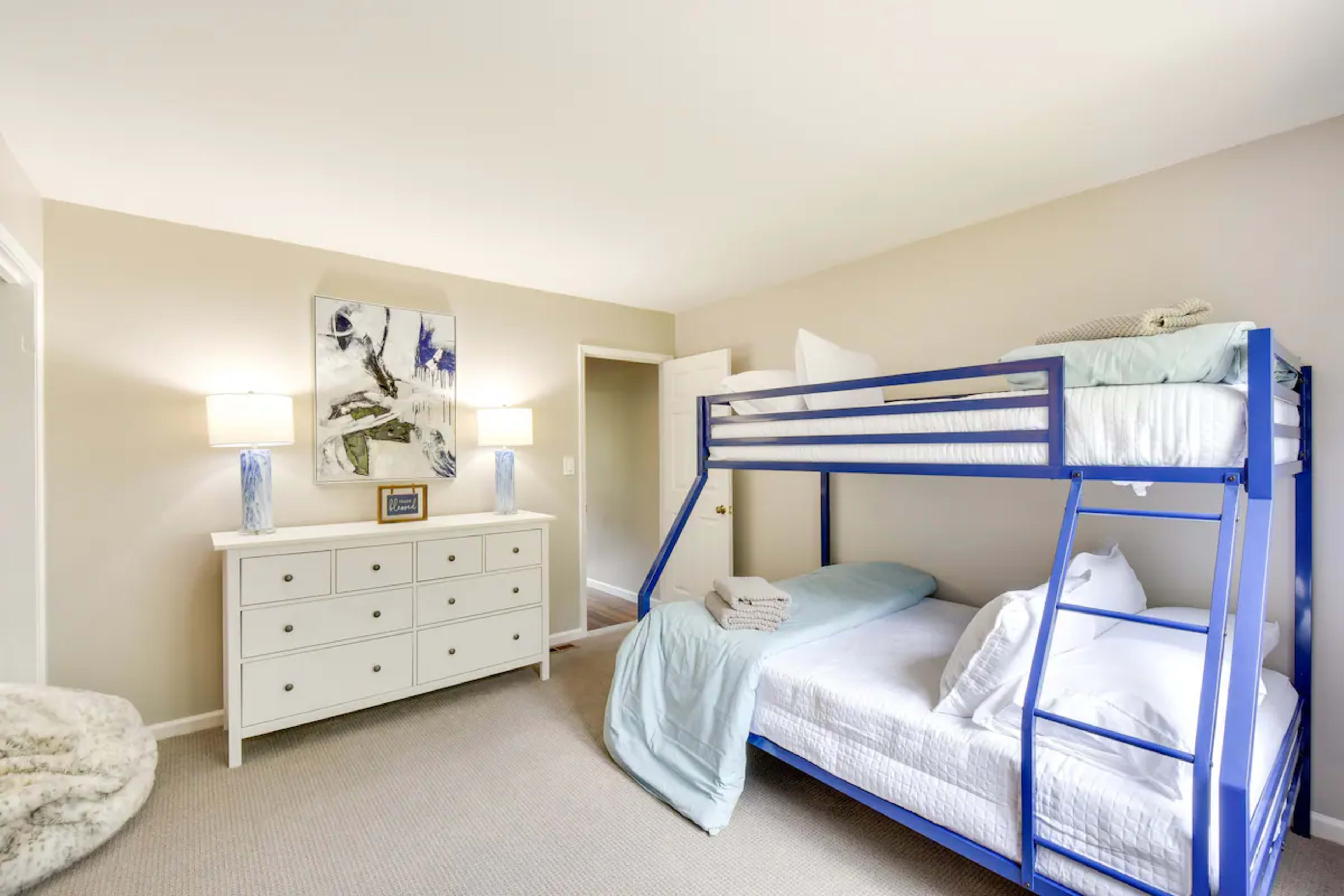 A bedroom with a blue bunk bed, a white dresser, and a pair of lamps on nightstands.