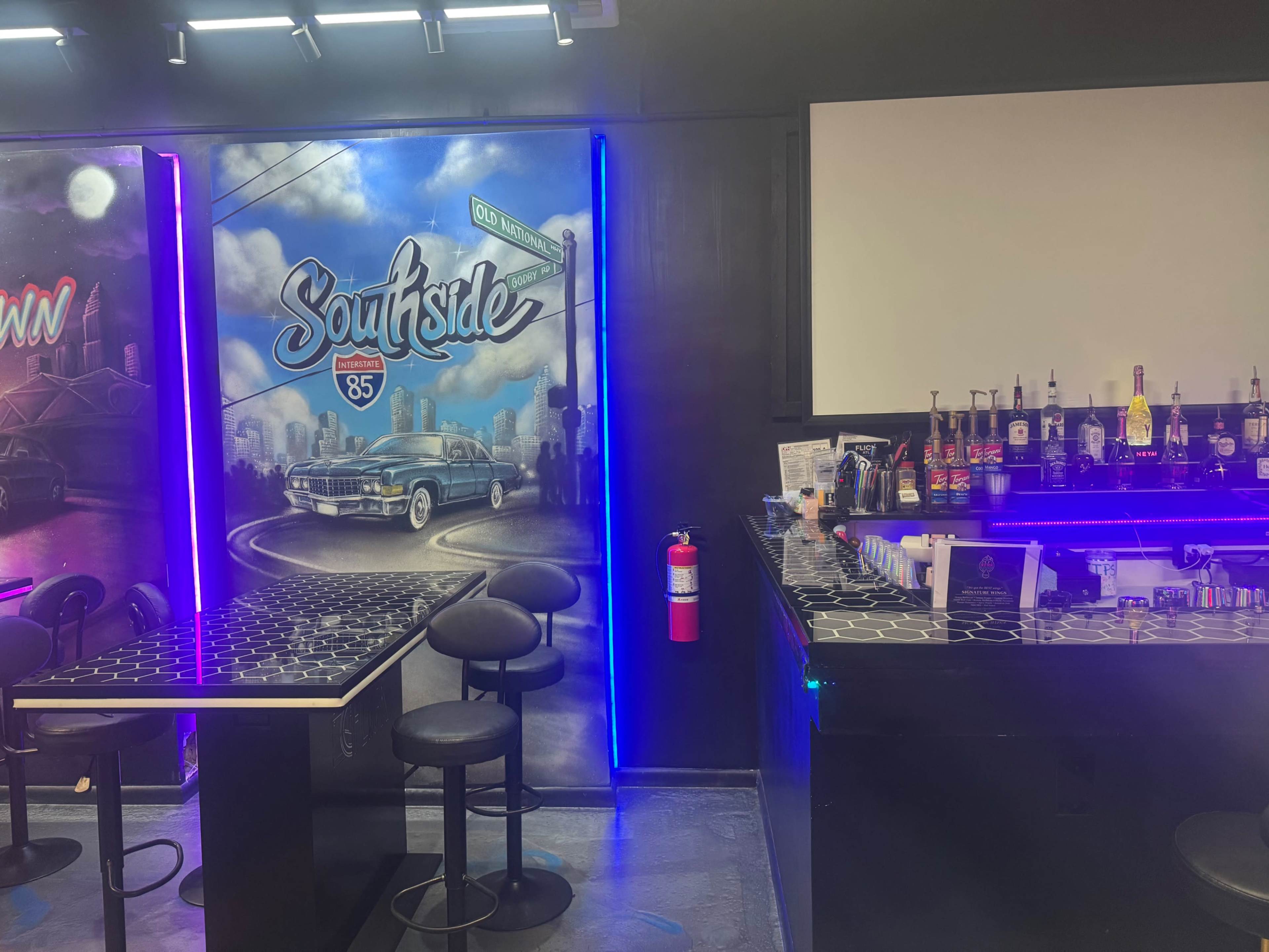 The image shows a bar area with a brightly lit backdrop featuring a mural of a classic car and the text "Southside 85," alongside a well-stocked bar with various bottles displayed.