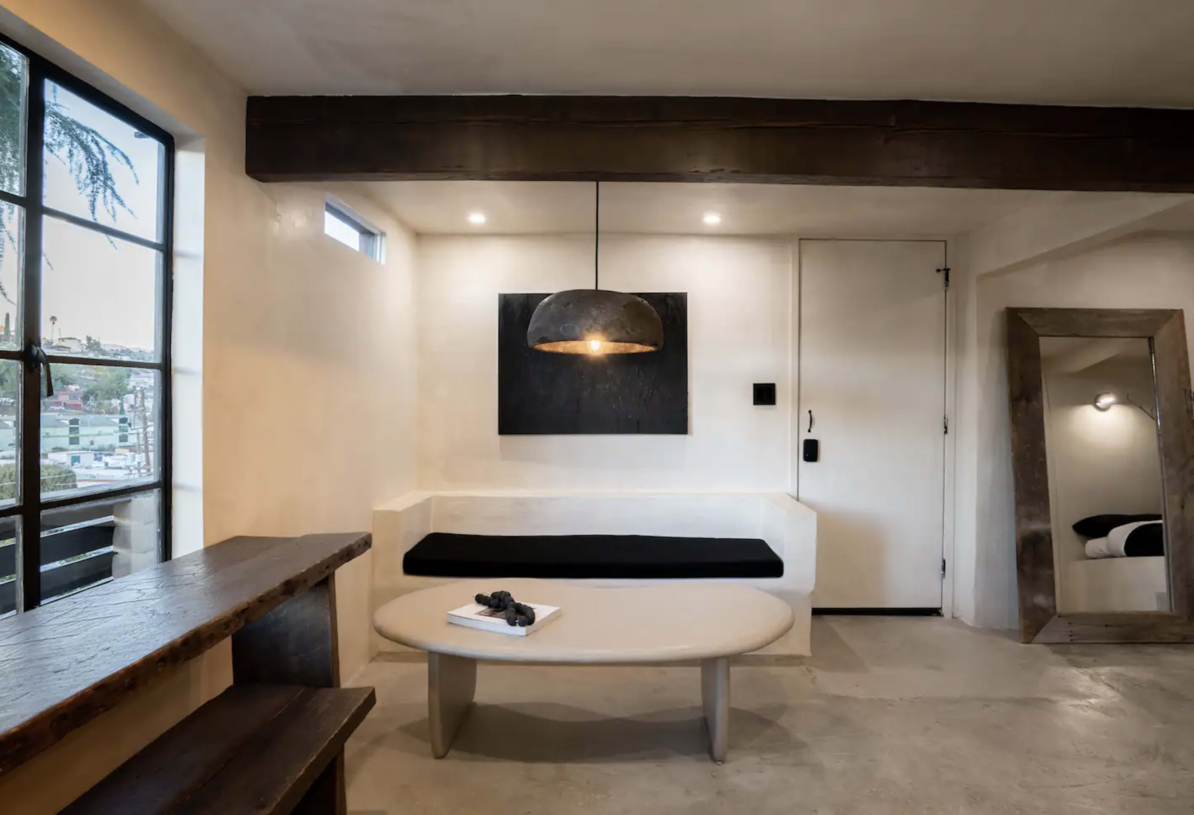 A minimalist living space featuring a light-colored wall, a curved seating area, a round coffee table, and a large pendant light above.