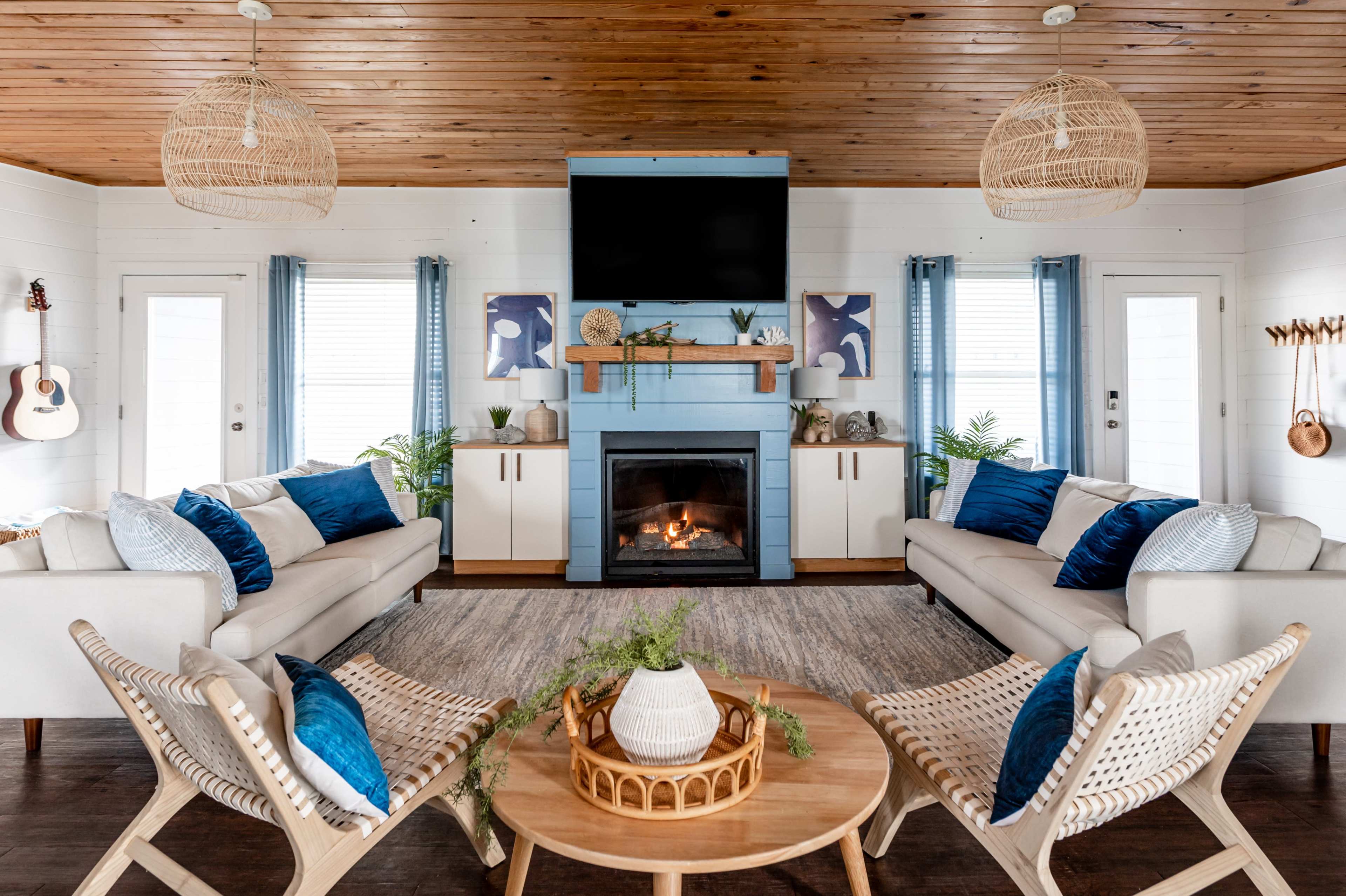 A modern living room with two sofas, a coffee table, a fireplace, and decorative plants, all surrounded by wooden paneling and large windows.