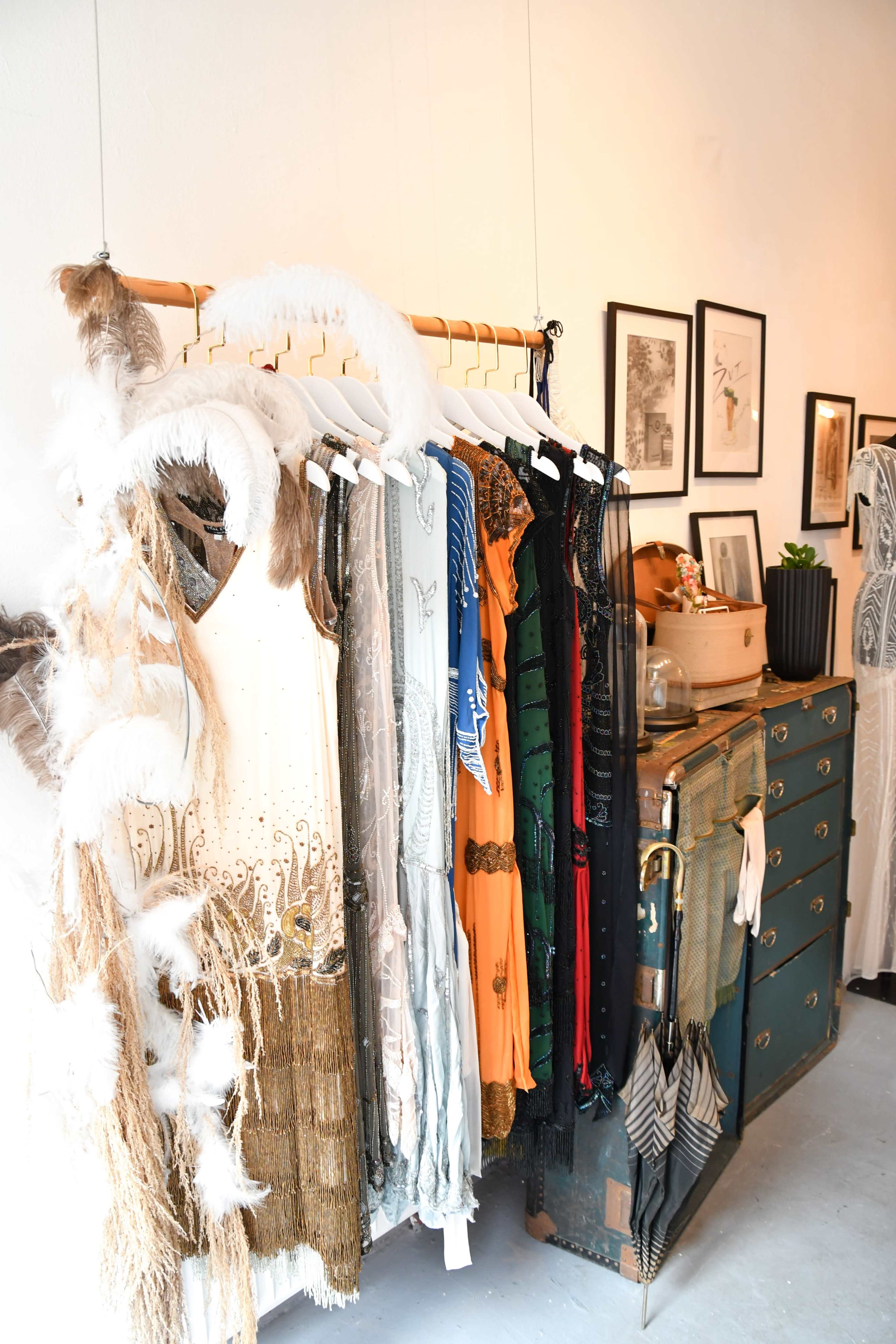 A clothing rack displays a variety of dresses, while a wooden dresser sits nearby with framed artwork on the walls.