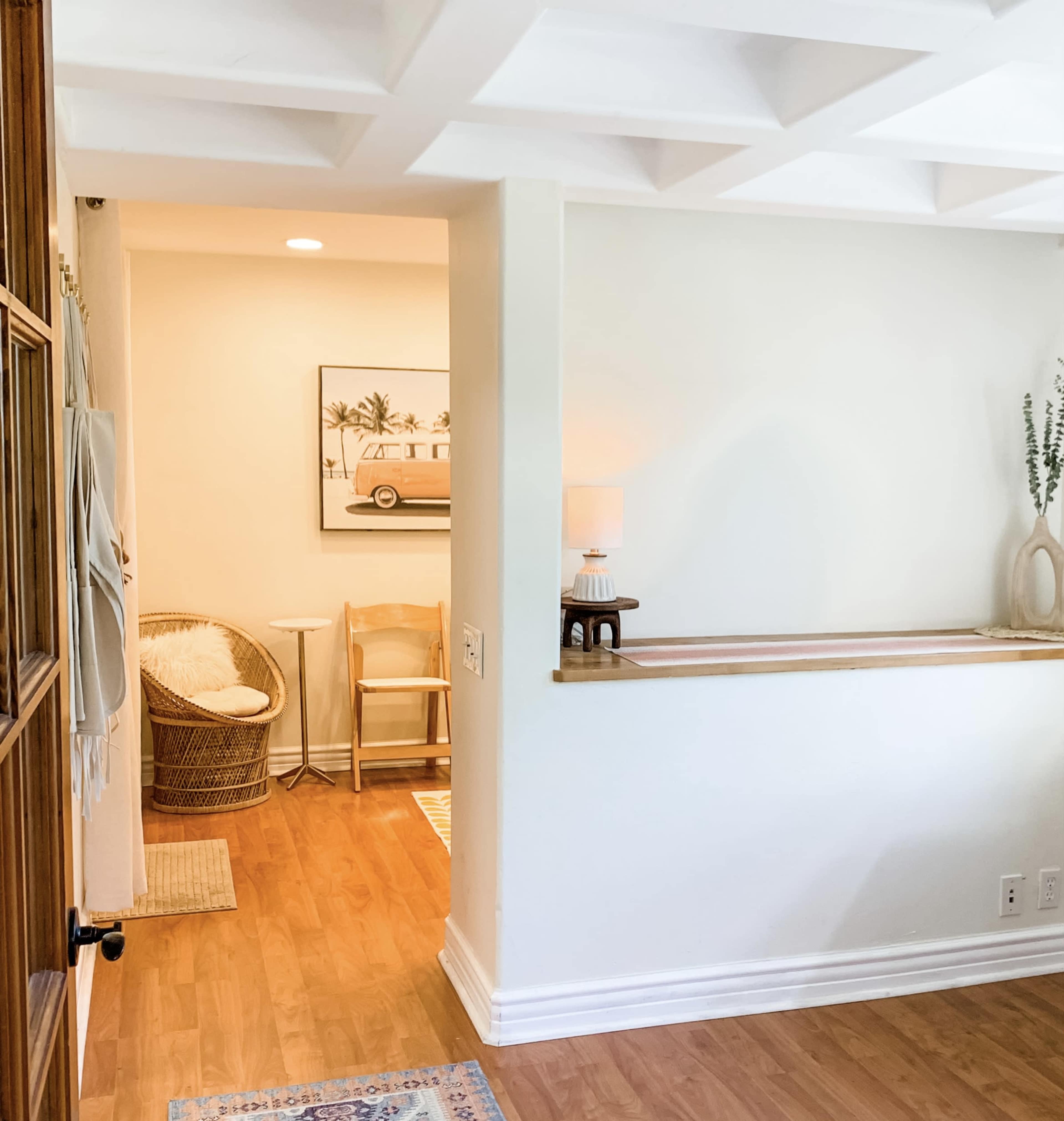 A well-lit entryway featuring a light-colored wall, wooden flooring, and a small bar area with a lamp and decorative items.