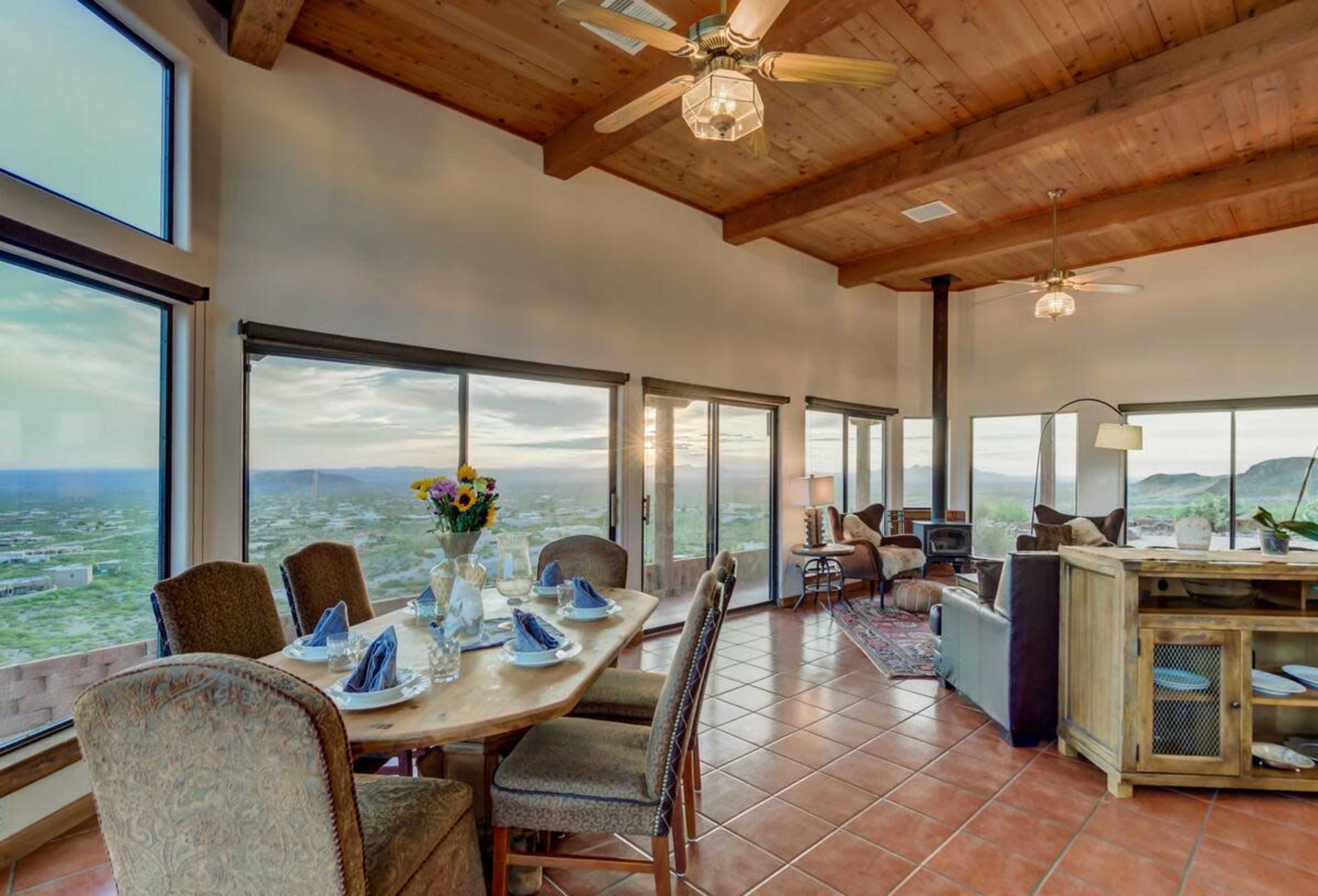 A dining area with a large table set for a meal and expansive windows showcasing a scenic view of the landscape beyond.