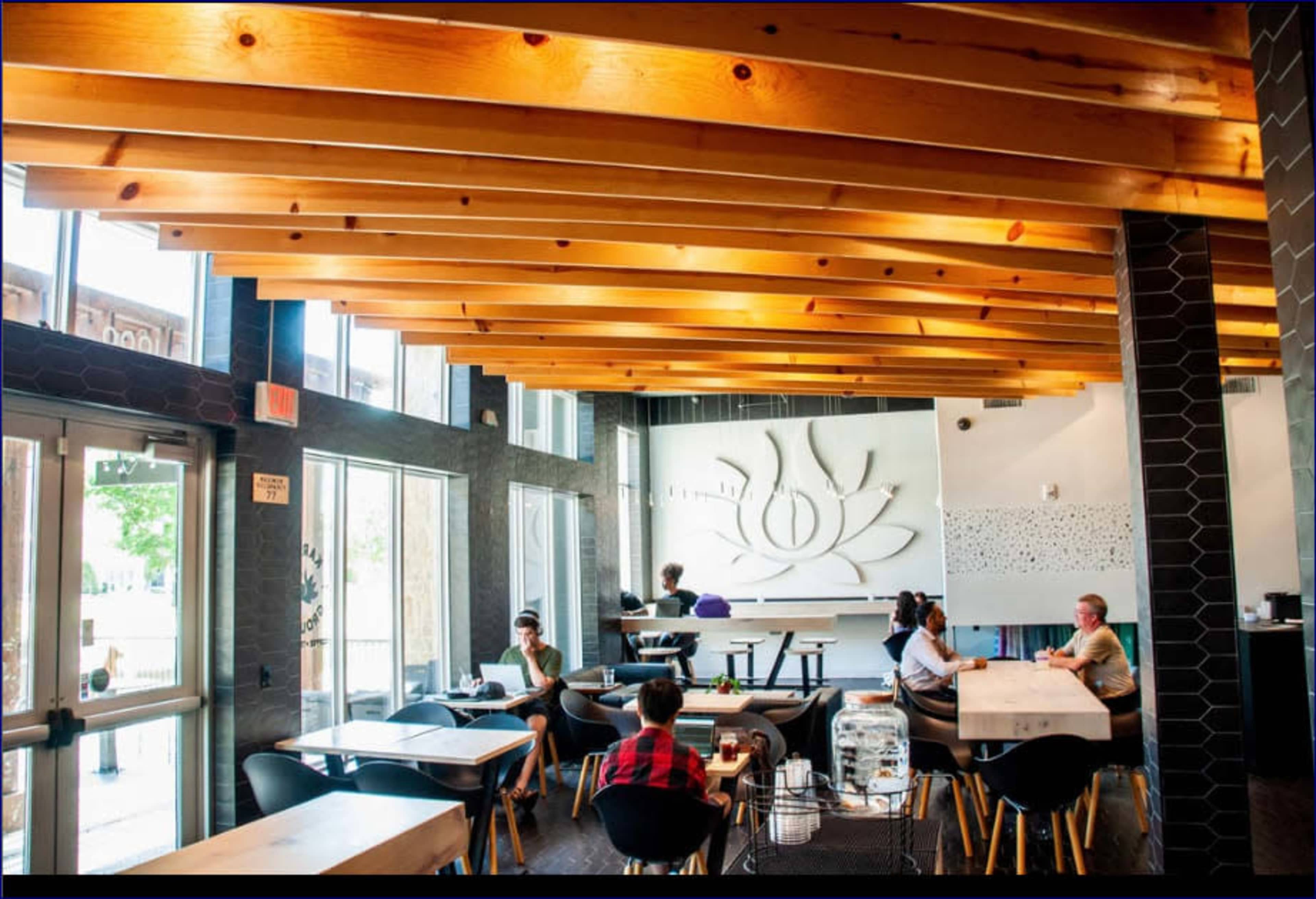 A modern cafe features wooden beams, minimalist decor, and patrons engaged in conversation at various tables.