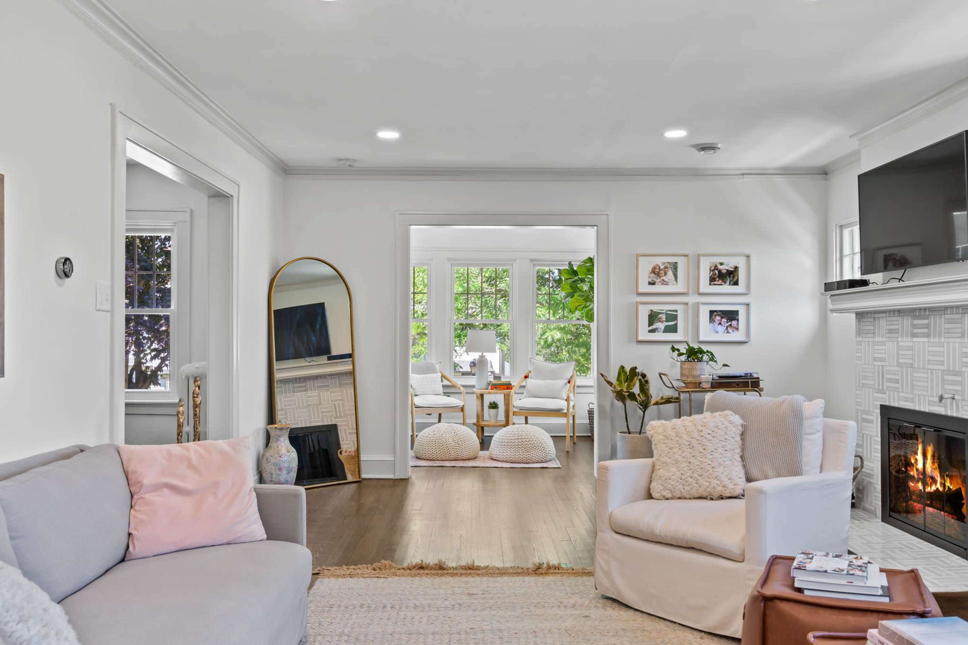 A cozy living room with a gray sofa, a white armchair, and a fireplace, leading to a bright dining area with a table and chairs partially visible.
