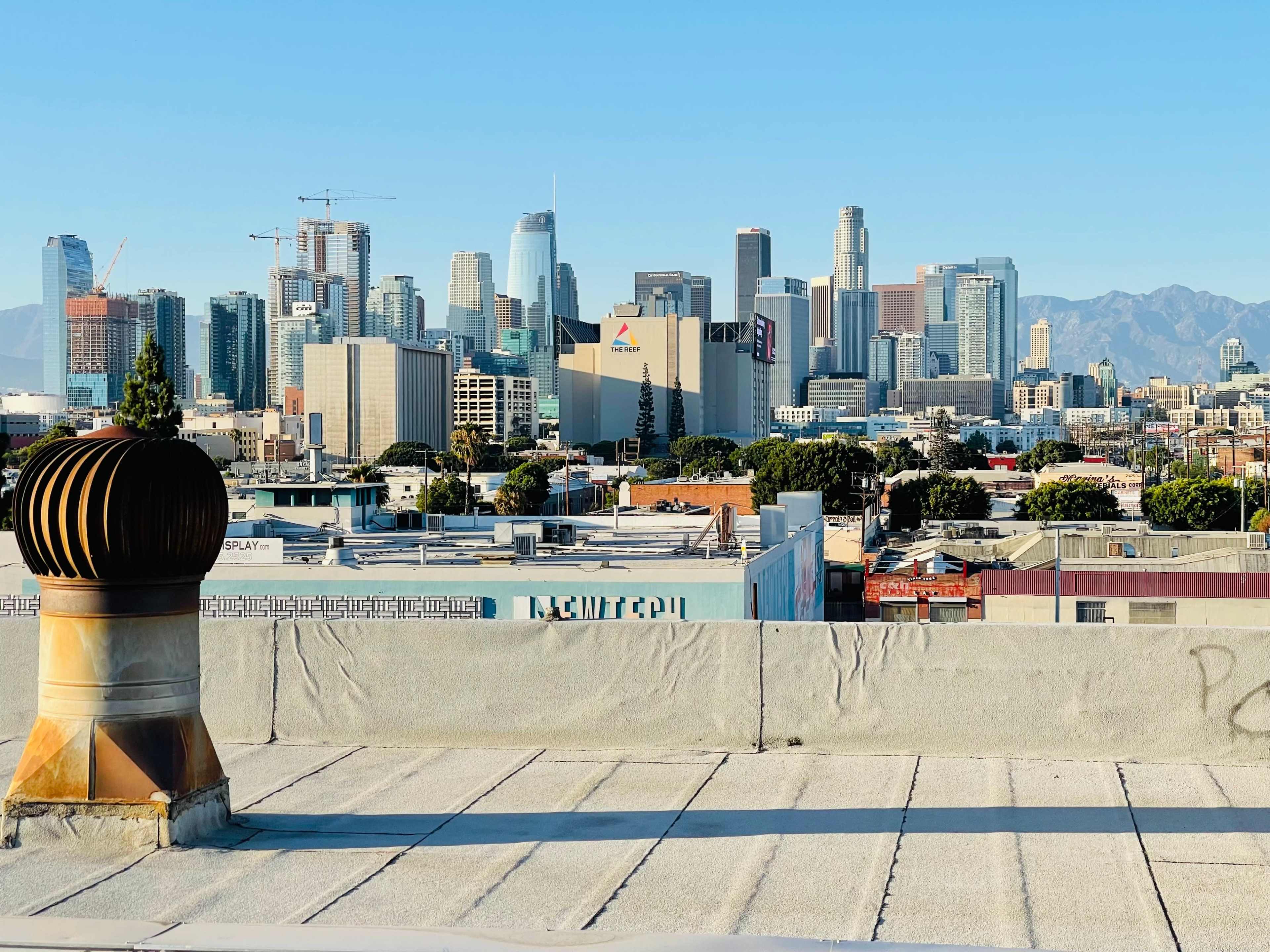 A rooftop view of downtown Los Angeles with skyscrapers in the background and industrial buildings in the foreground.