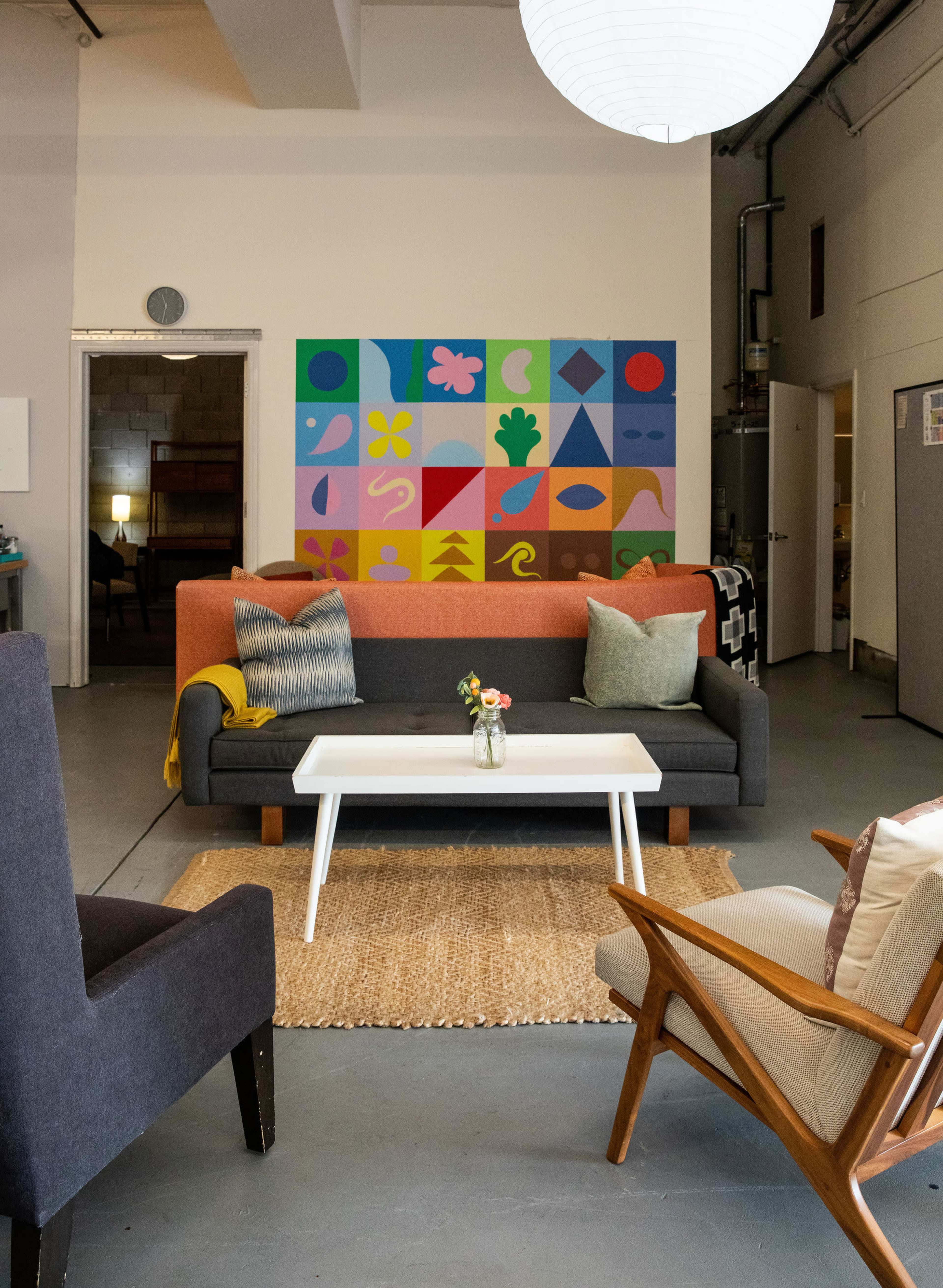 The image shows a modern living space with a colorful mural on the wall, a two-tone sofa, a coffee table, and various seating arrangements.